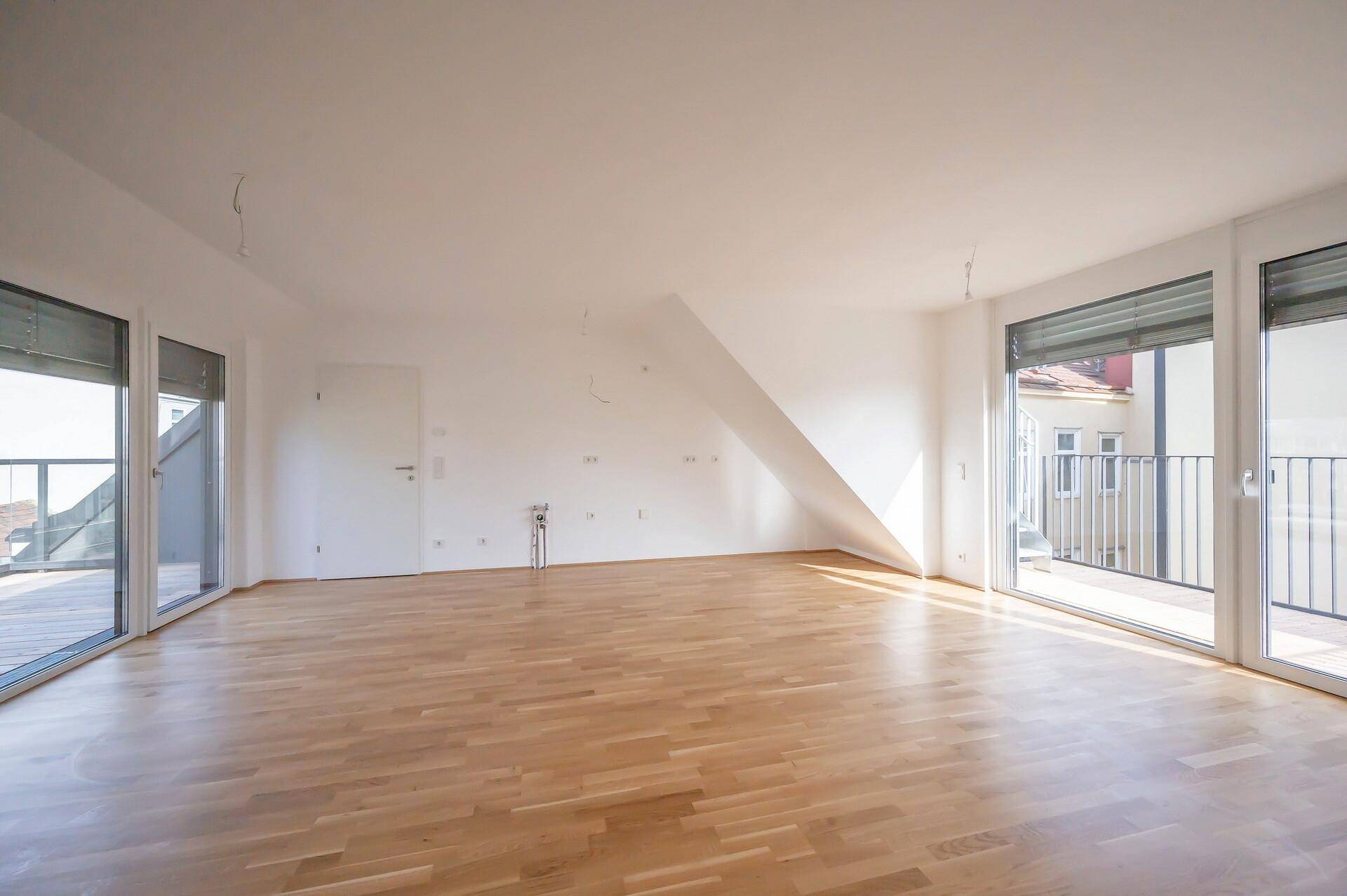 Lichtdurchfluteter Raum mit Holzboden und mehreren Fenstertüren, die zu Balkonen führen.