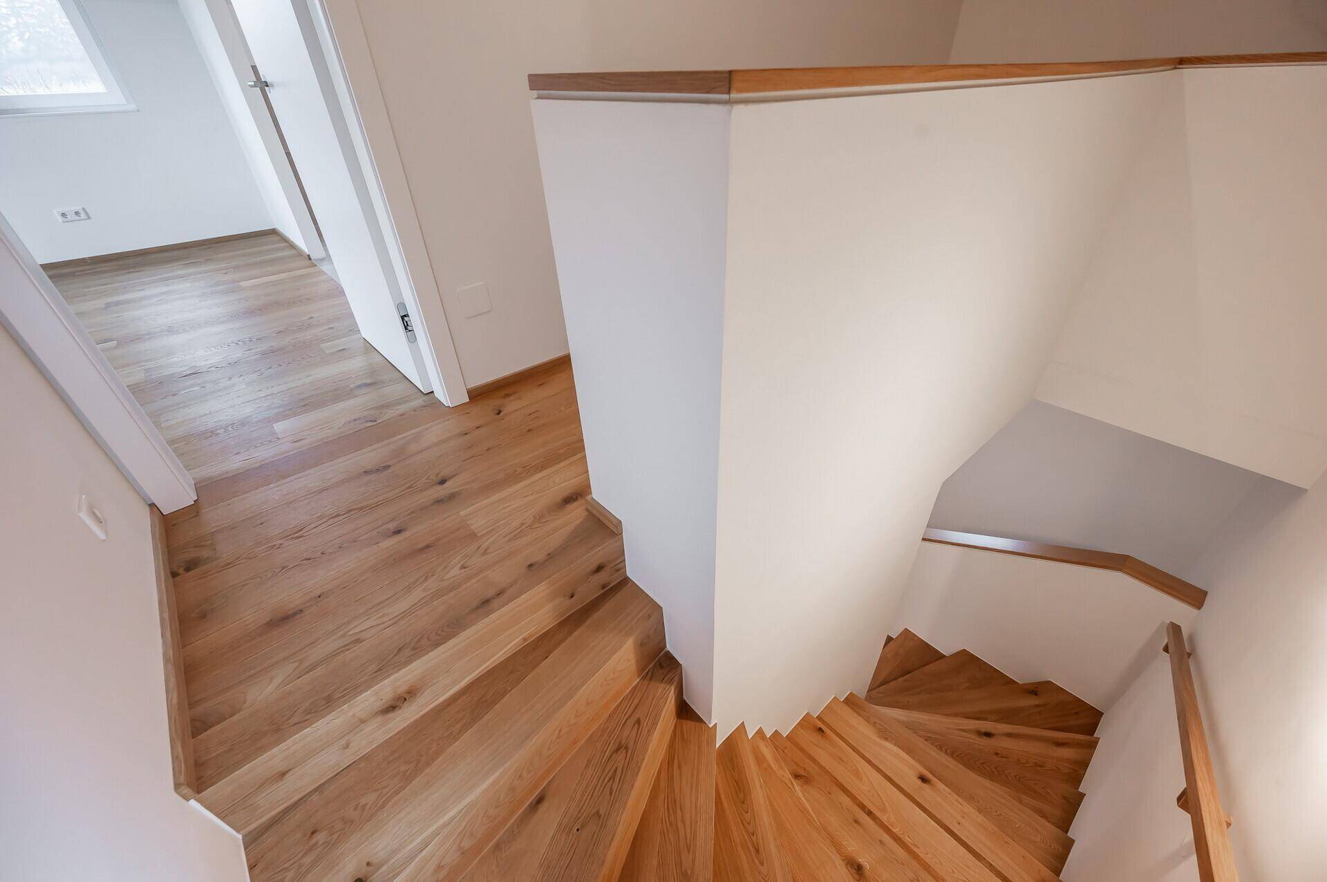 Blick von oben auf die geschwungene Holztreppe mit hellem Holzboden.