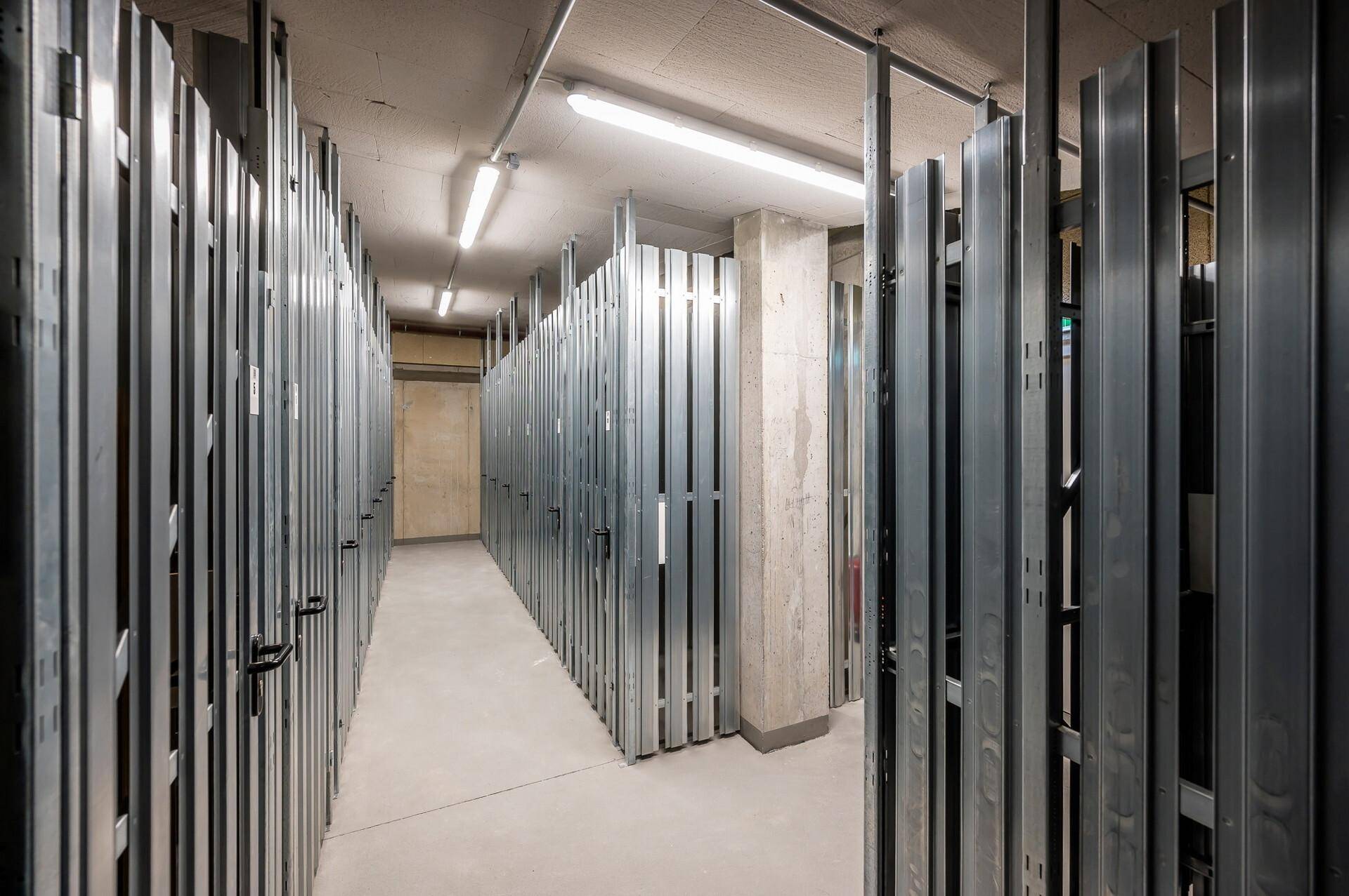Lagerräume im Untergeschoss mit Metallabtrennungen und Betonboden, gut beleuchtet.