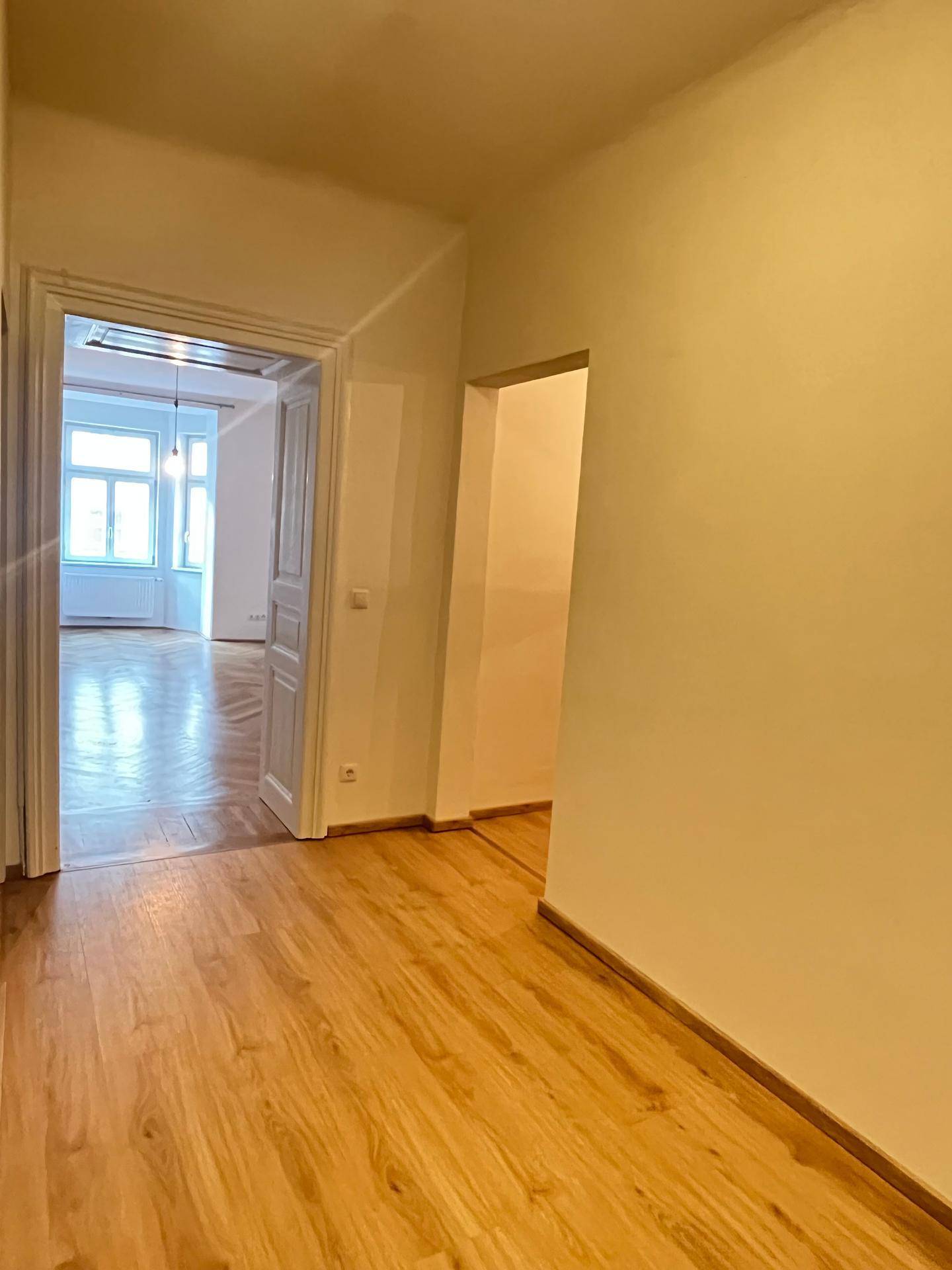 Gangbereich mit Laminatboden und Blick in ein helles Zimmer mit Parkettboden.