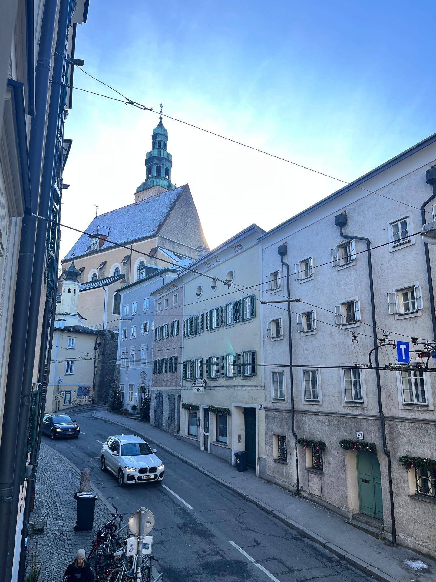 Historische Gasse mit traditionellen Gebäuden und einer Kirche im Hintergrund unter blauem Himmel.