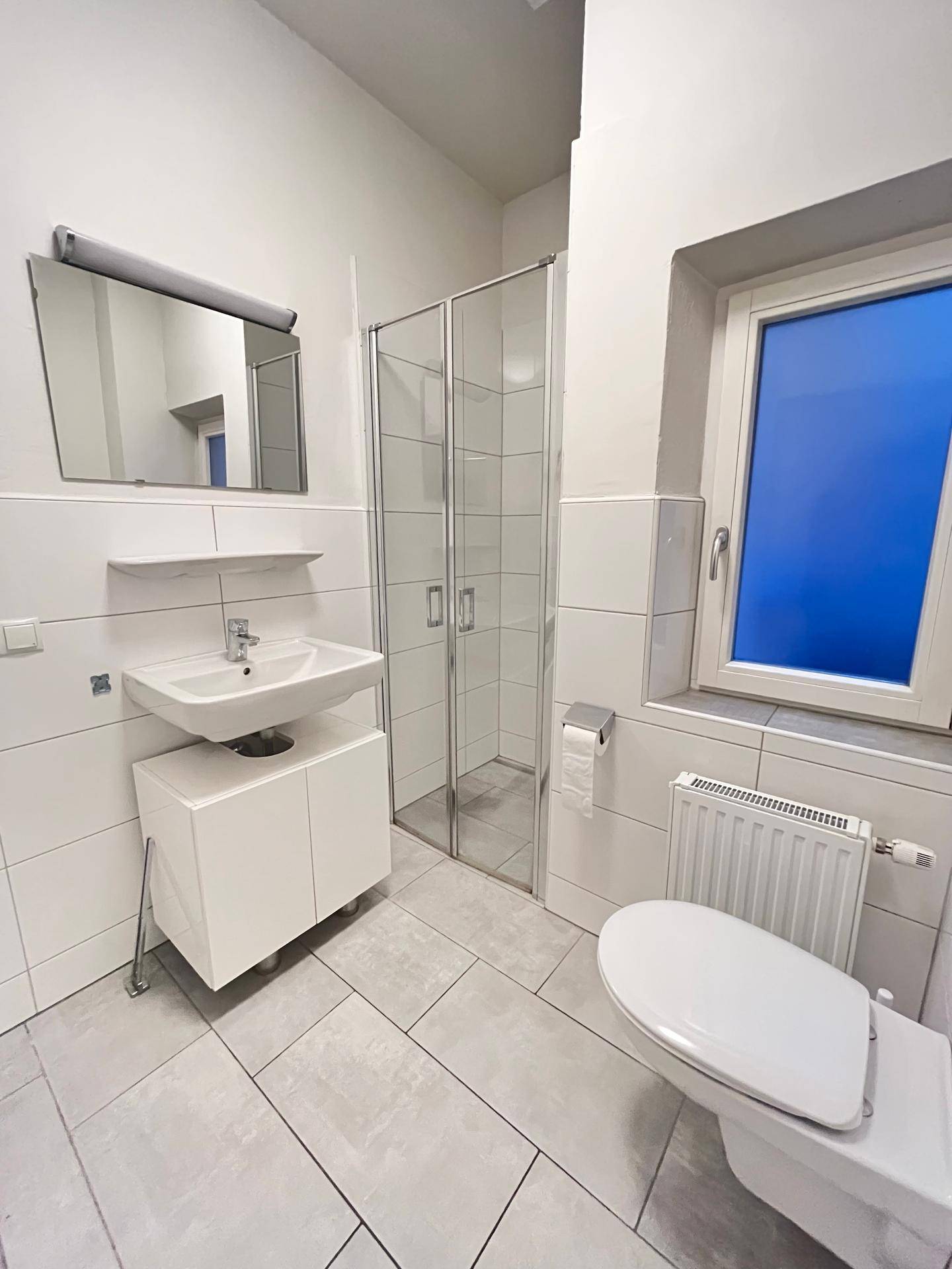 Modernes Badezimmer mit Dusche, WC und Waschbecken, hell gefliest und mit Fenster.