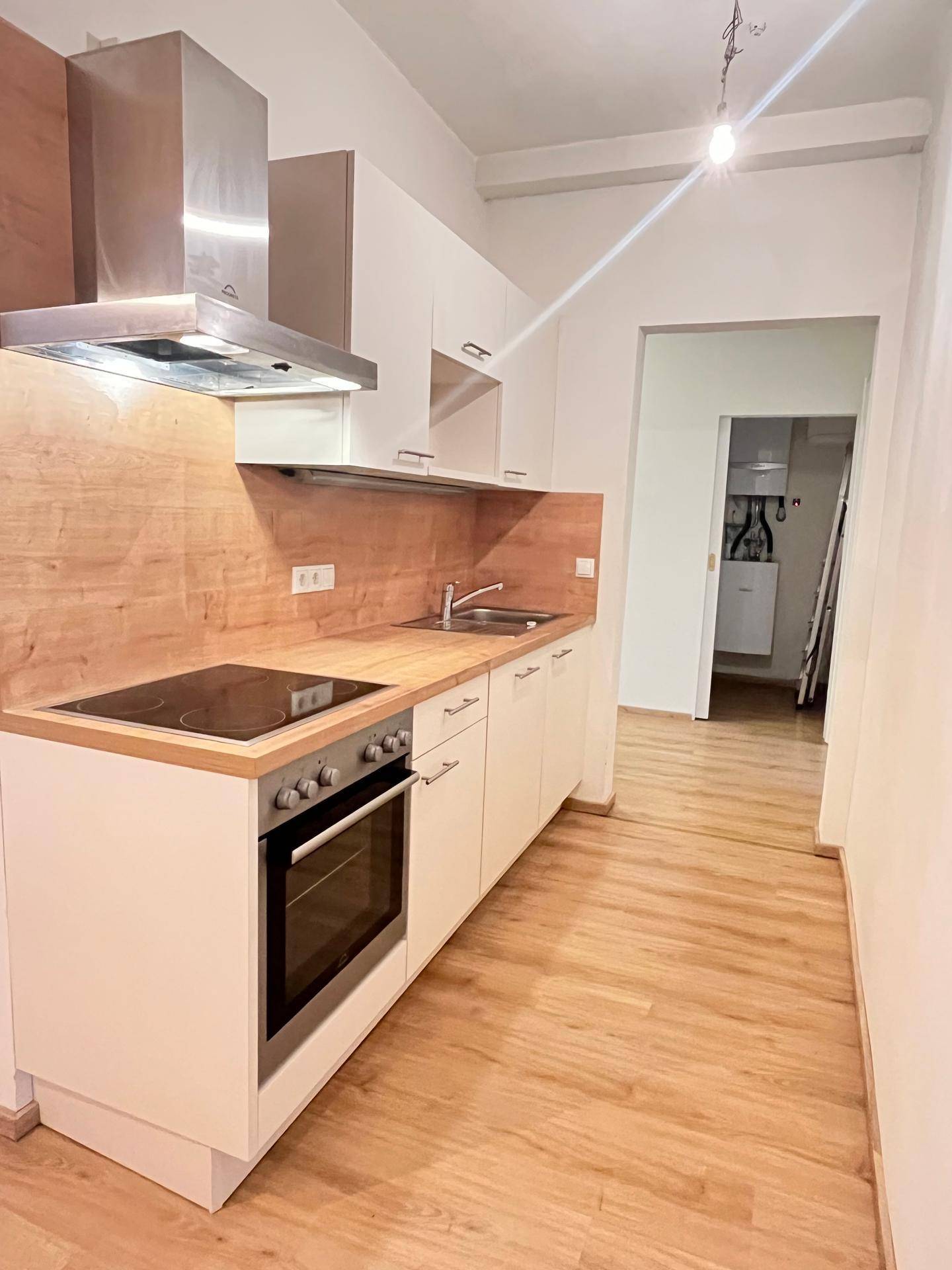 Moderne Einbauküche mit Holzoptik-Arbeitsplatte und Edelstahl-Dunstabzugshaube, hell und funktional.