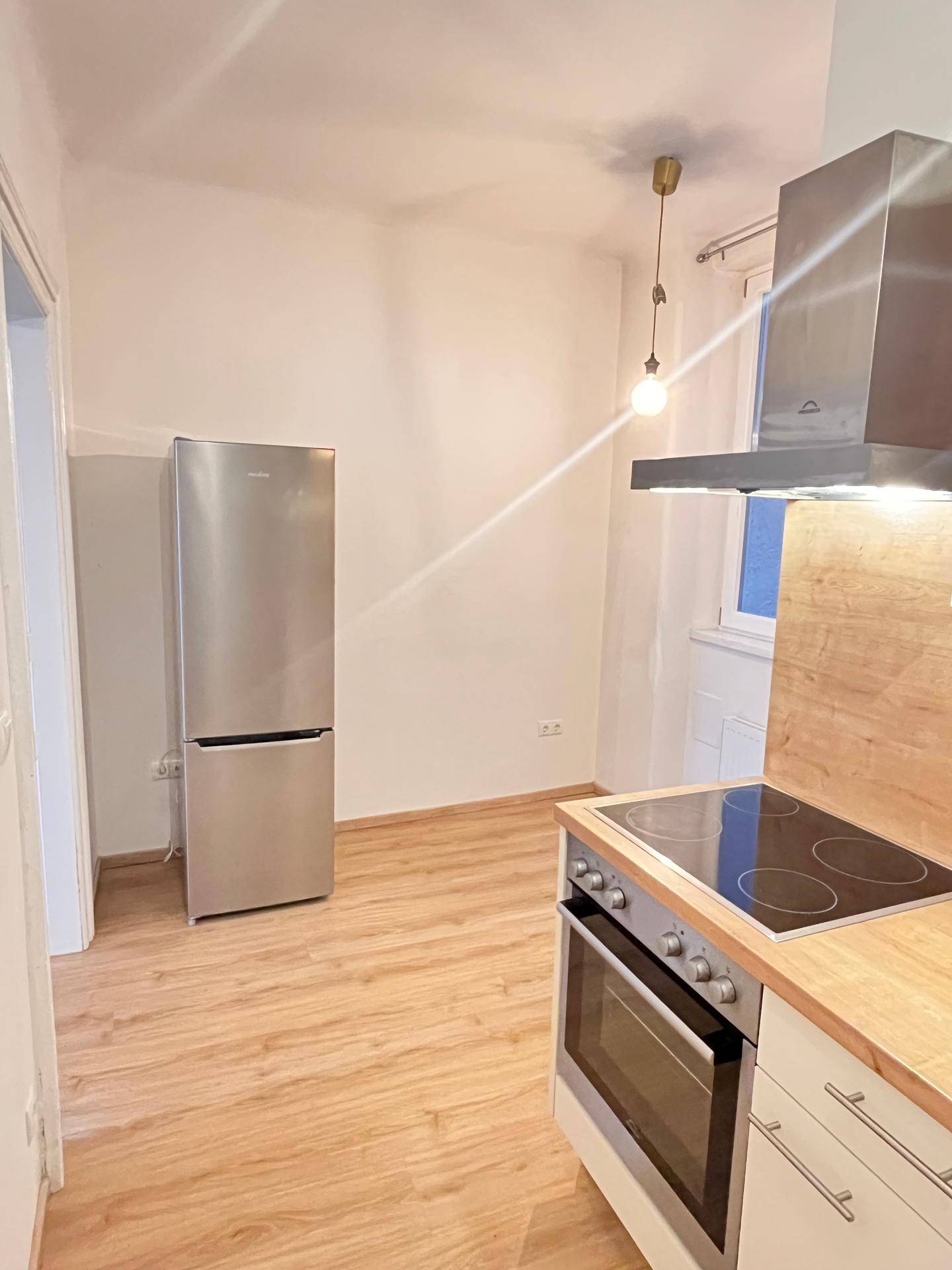 Funktionale Küche mit freistehendem Kühlschrank, Herd und Dunstabzugshaube, bereit zur Nutzung.