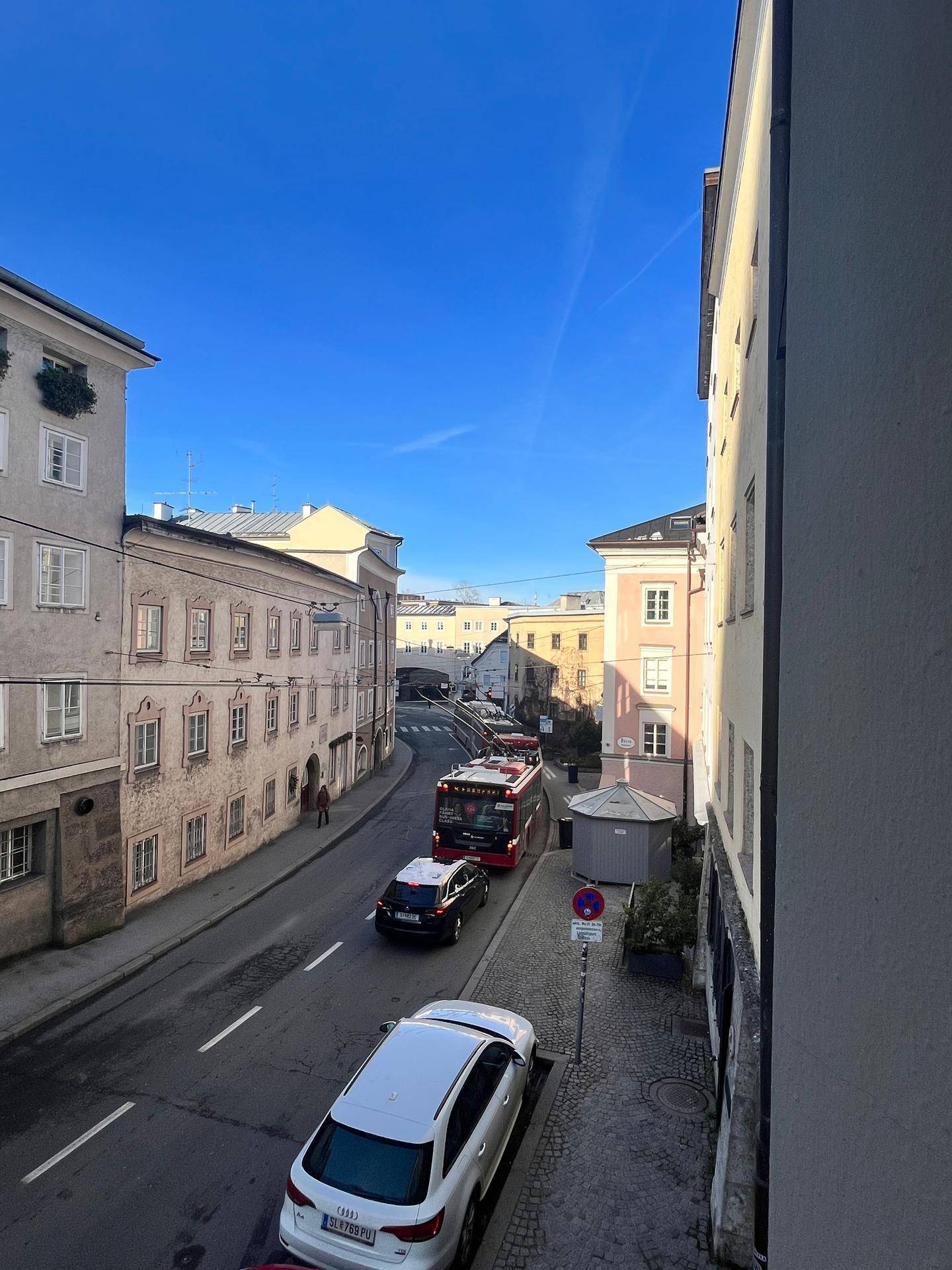 Belebte Stadtansicht mit Gebäuden, Fahrzeugen und Fußgängern unter klarem blauem Himmel.