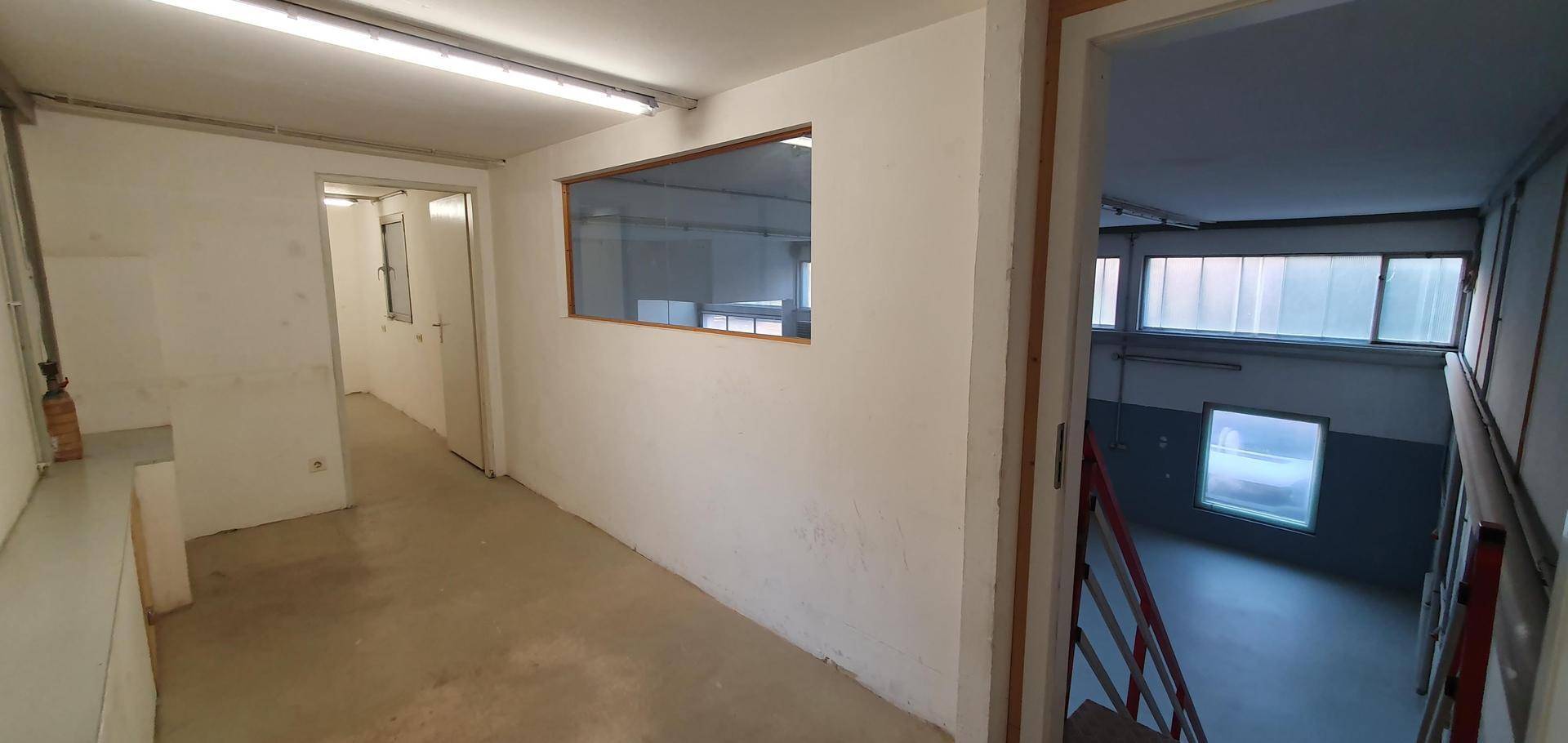 Flur mit weiß gestrichenen Wänden, einem Fenster zur Halle und Zugang zu weiteren Räumen.
