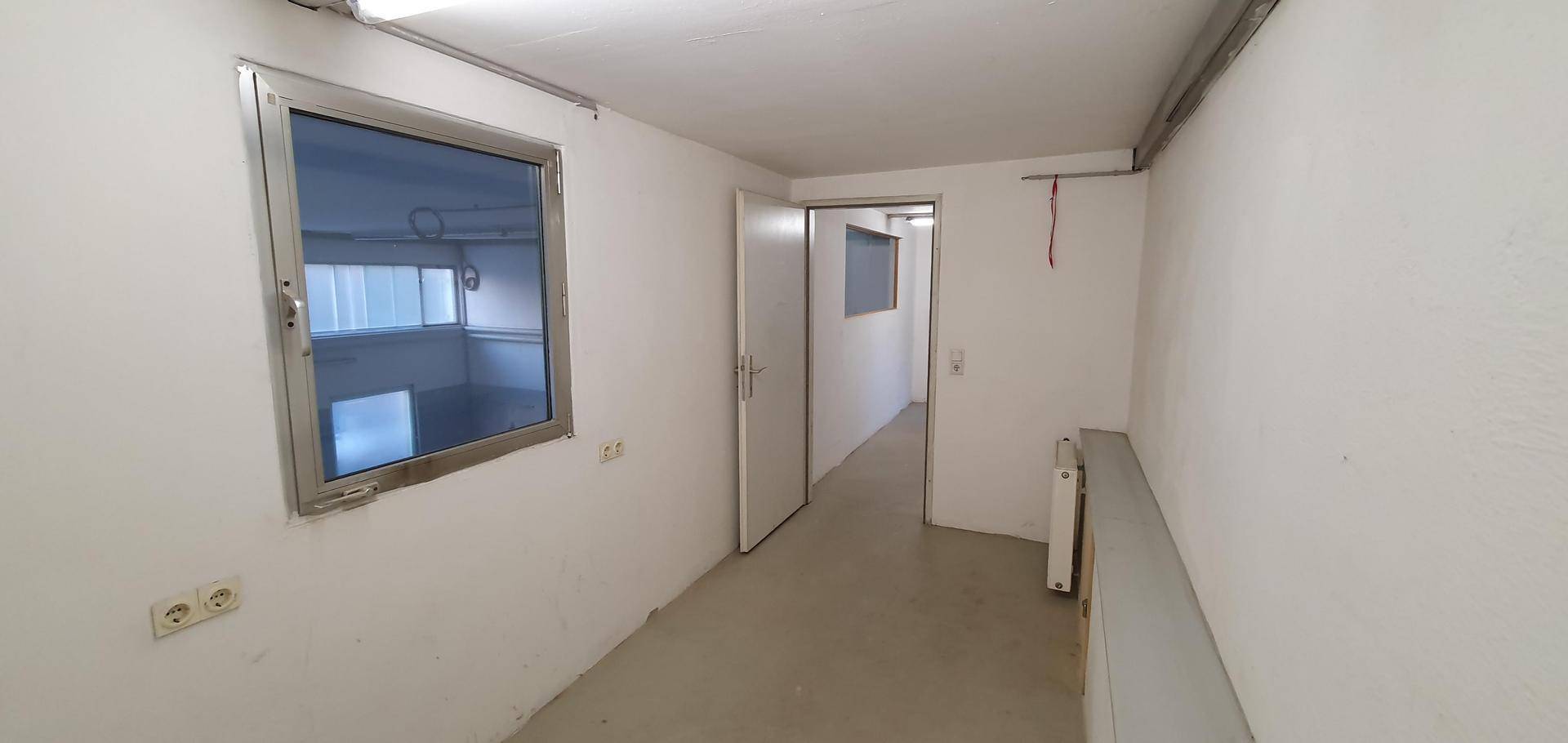 Heller Büroraum mit einem Fenster, weißen Wänden und einem einfachen Heizkörper.