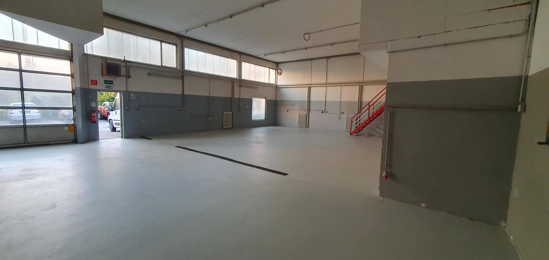 Weitläufige Werkshalle mit einem großen Rolltor und einer roten Treppe im hinteren Bereich.