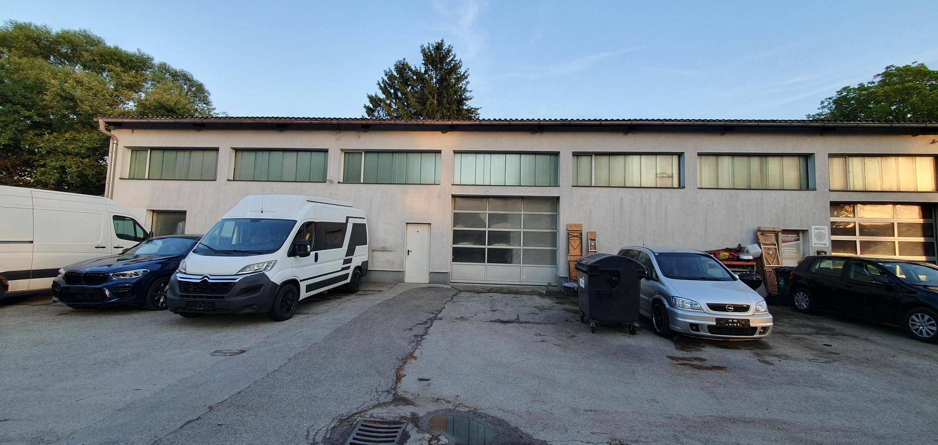 Fassade eines Gewerbegebäudes mit großen Fenstern und mehreren geparkten Lieferwagen und Autos.