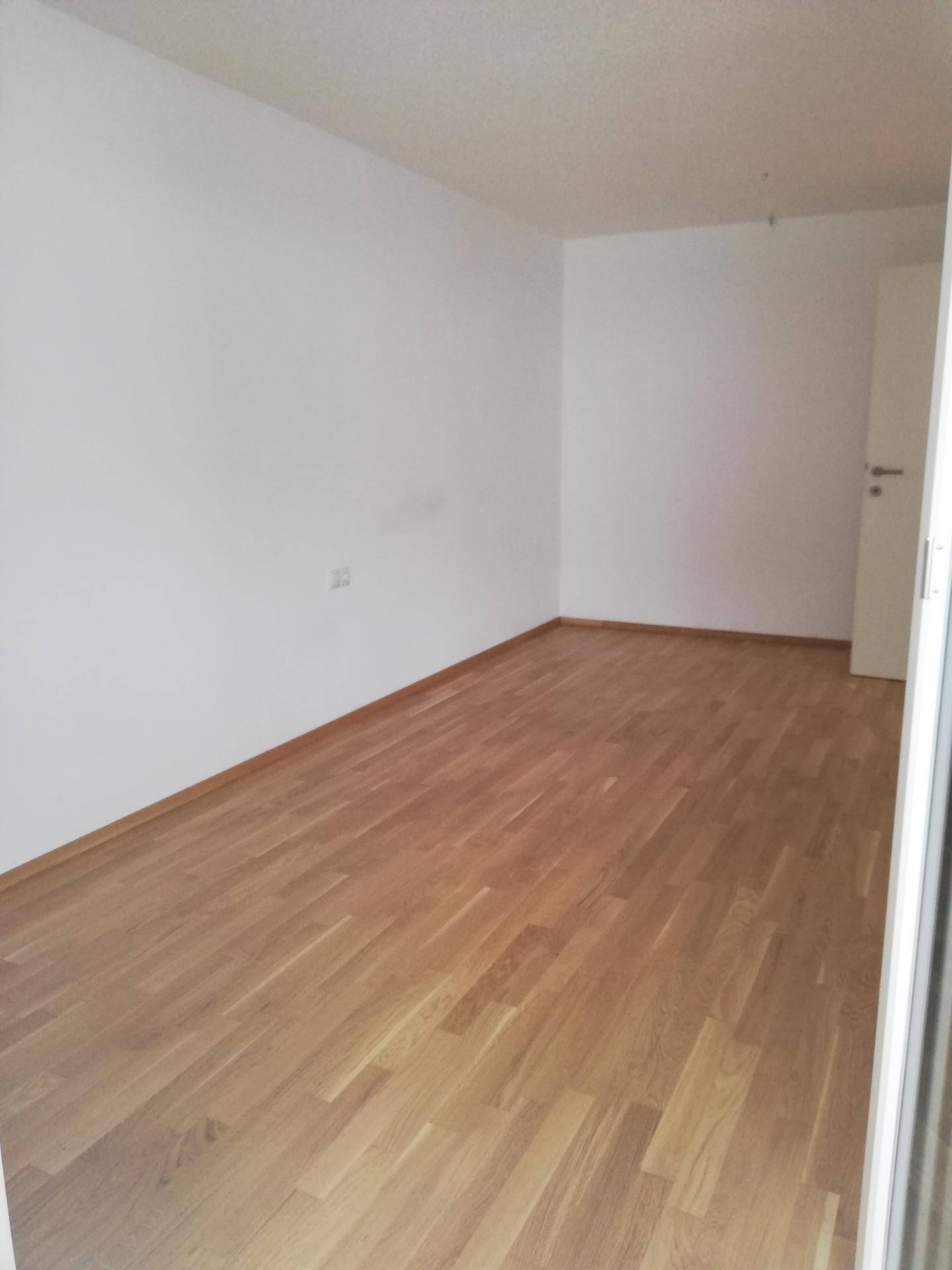 Leeres Schlafzimmer mit hellem Holzboden und weißen Wänden, ideal für persönliche Einrichtung.