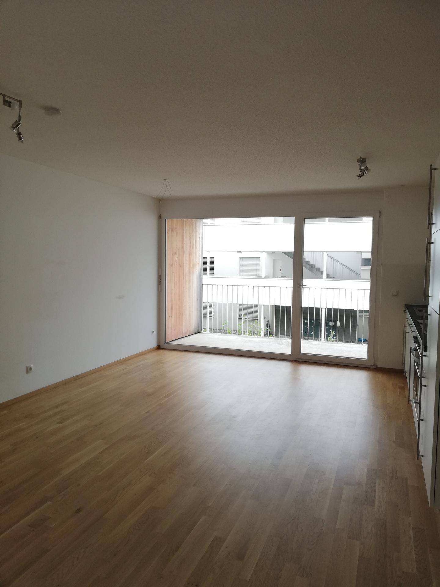 Heller Wohnbereich mit großen Fenstern und Zugang zu einem Balkon mit Blick nach draußen.