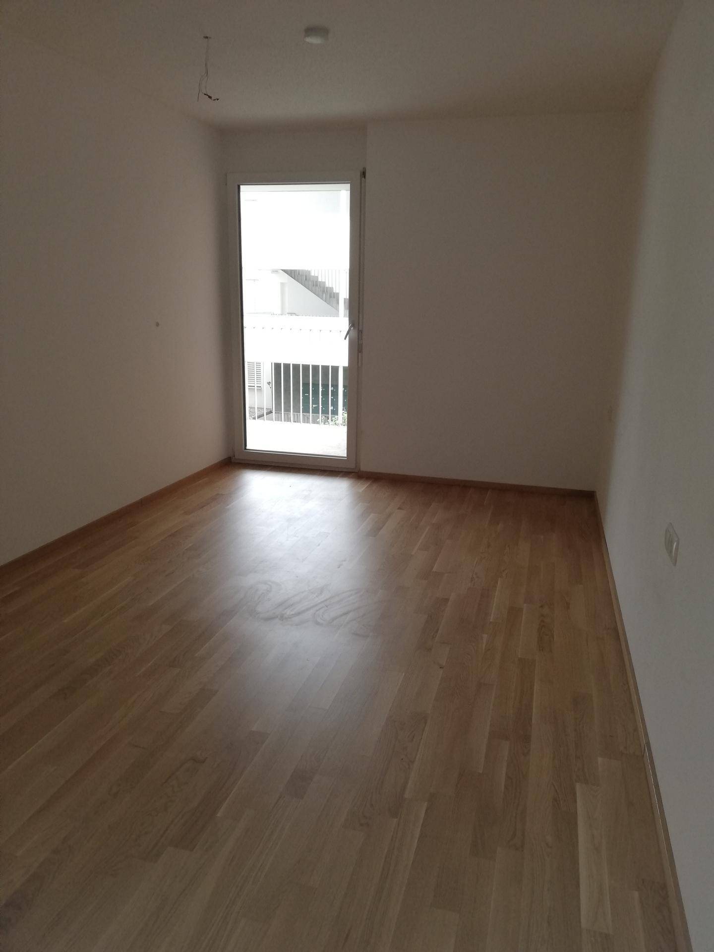 Schlafzimmer mit hellem Parkettboden und Zugang zu einem französischen Balkon.