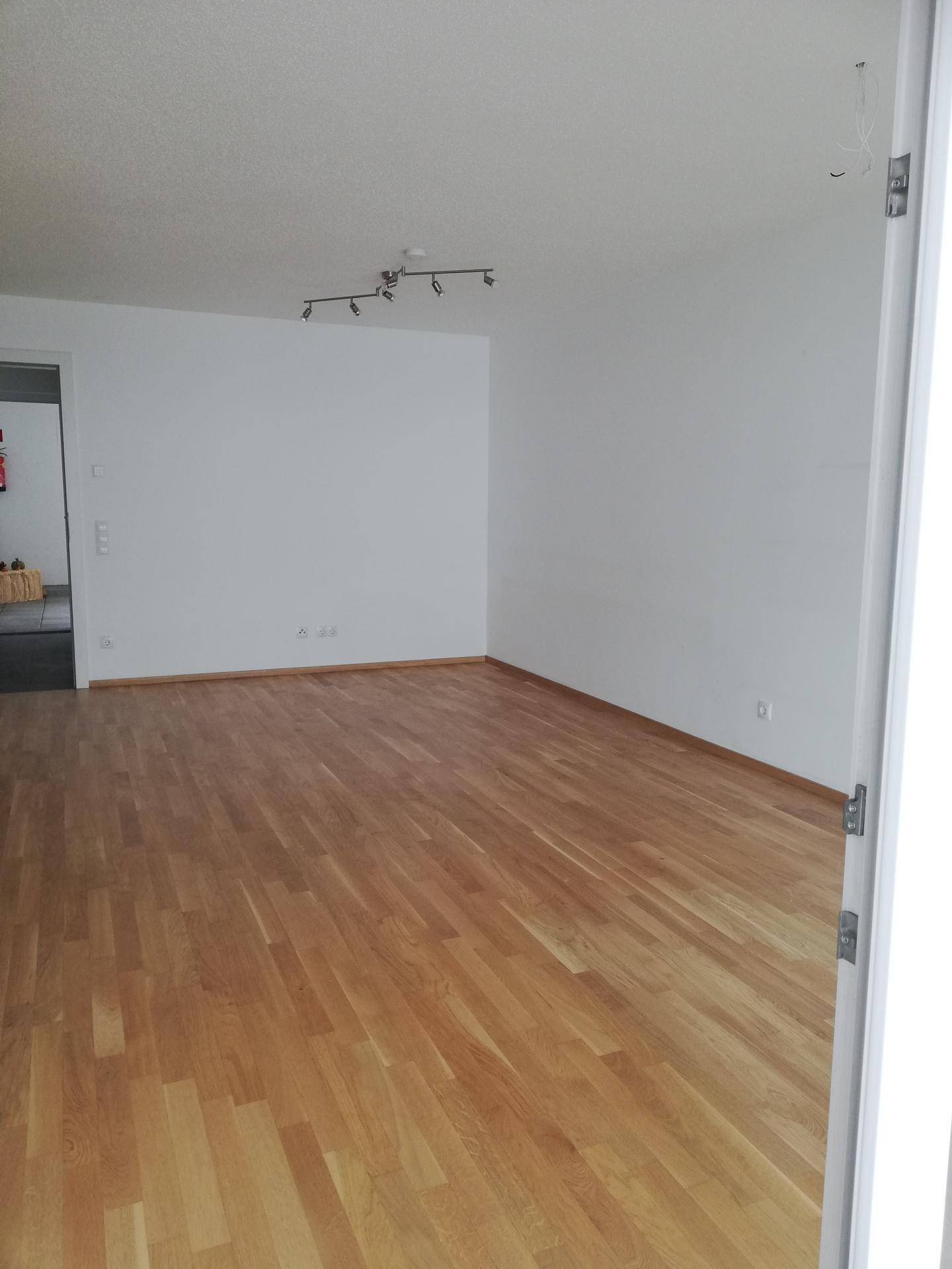 Leeres Wohnzimmer mit hellem Parkettboden und weißen Wänden, bereit zur individuellen Gestaltung.