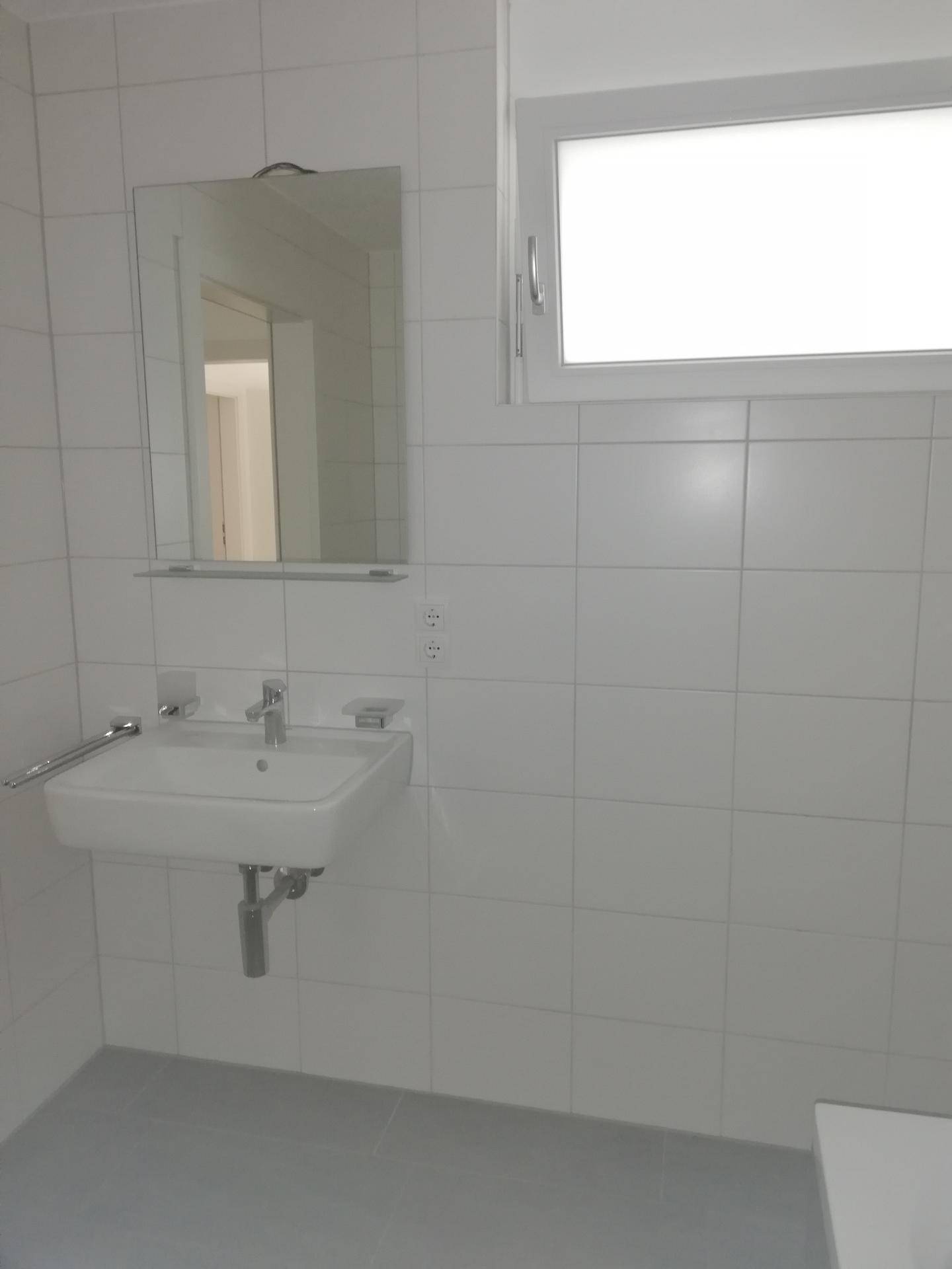 Helles Badezimmer mit Waschbecken, Spiegel und einem Fenster für natürliches Tageslicht.