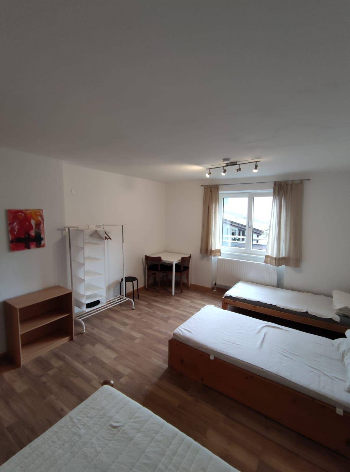 Geräumiges Schlafzimmer mit drei Einzelbetten, kleinem Tisch und Fenster für natürliche Belichtung.