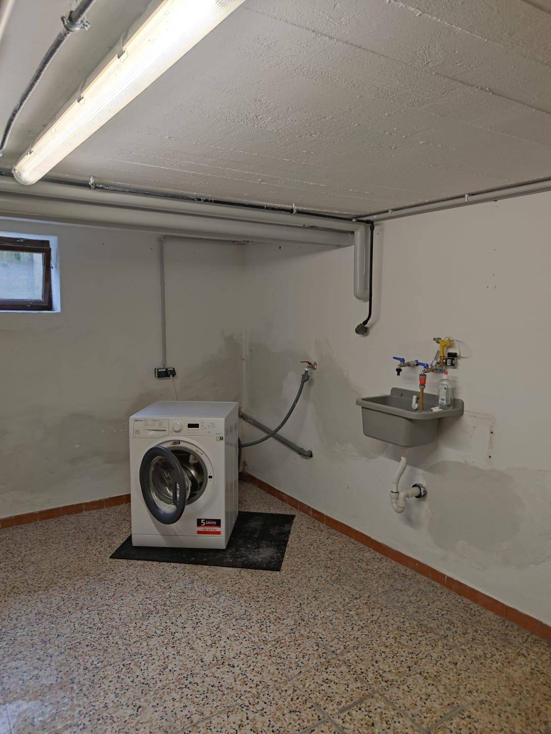 Praktischer Hauswirtschaftsraum im Keller mit Waschmaschine, Spülbecken und kleinem Fenster.