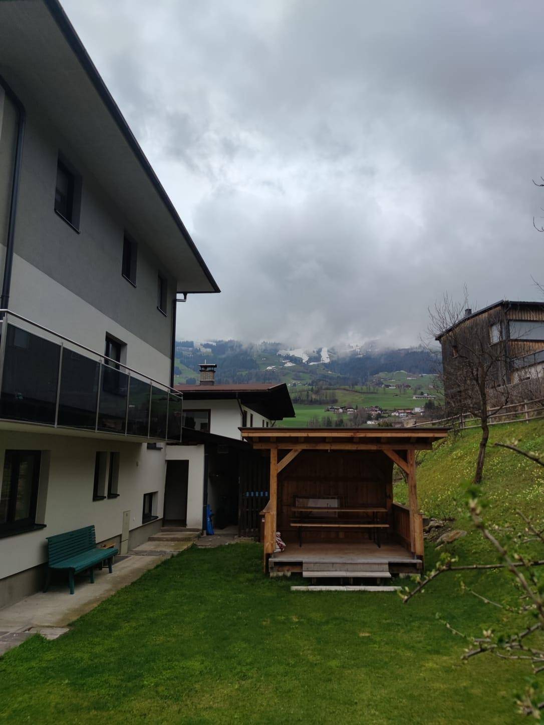 Seitenansicht des Gebäudes mit Holzpavillon im Garten und malerischem Blick auf die Berge.
