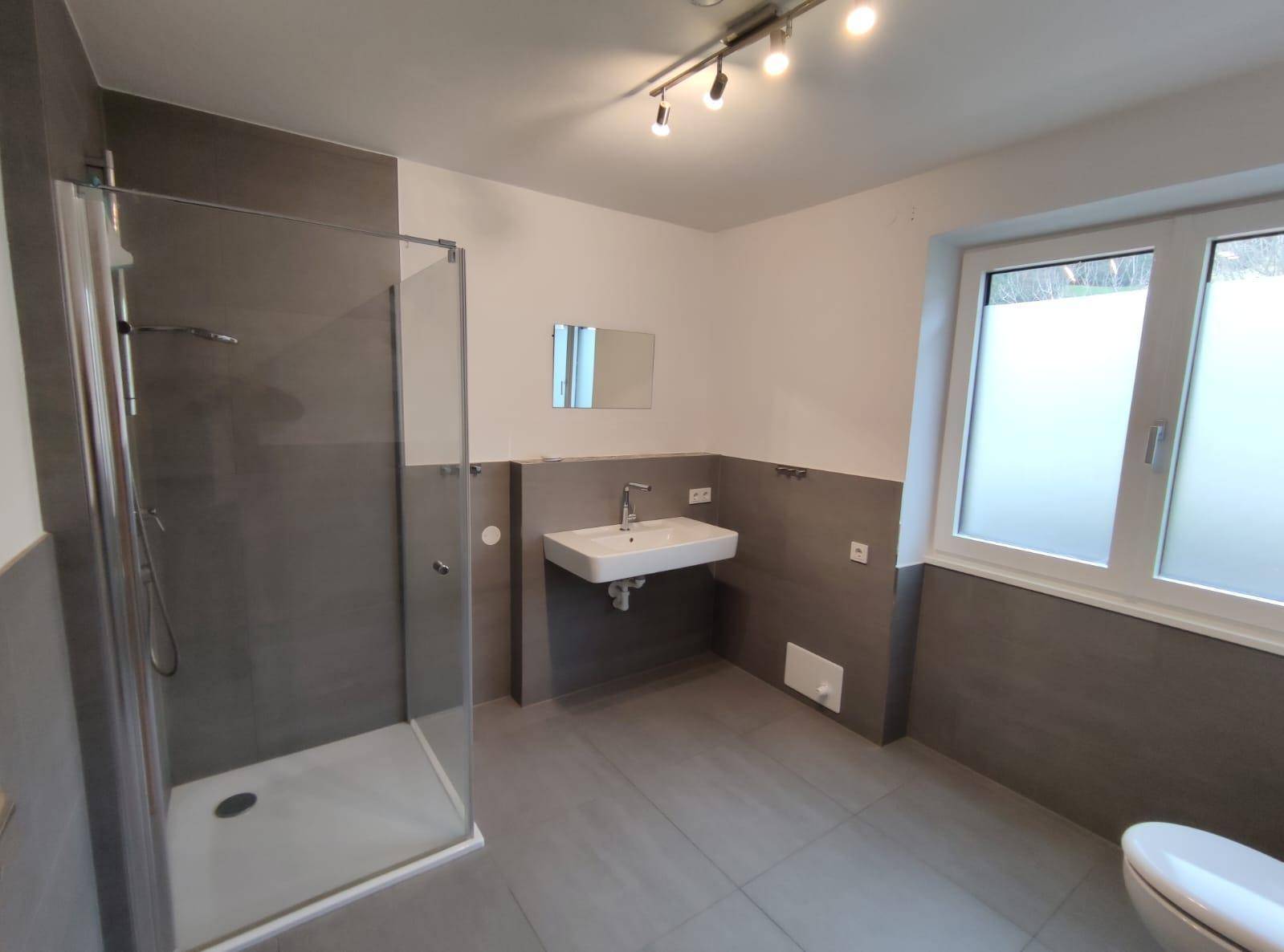 Modernes Badezimmer mit ebenerdiger Dusche, Waschbecken und Fenster für Tageslicht.