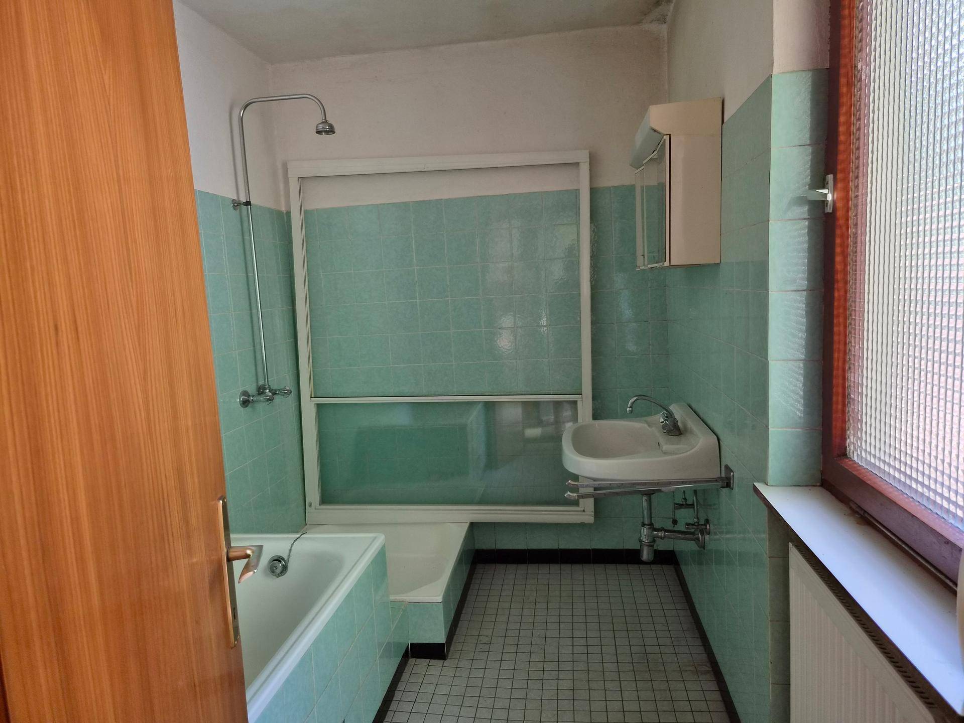Badezimmer im Stil der 80er Jahre mit hellgrünen Fliesen, Badewanne und Waschbecken.