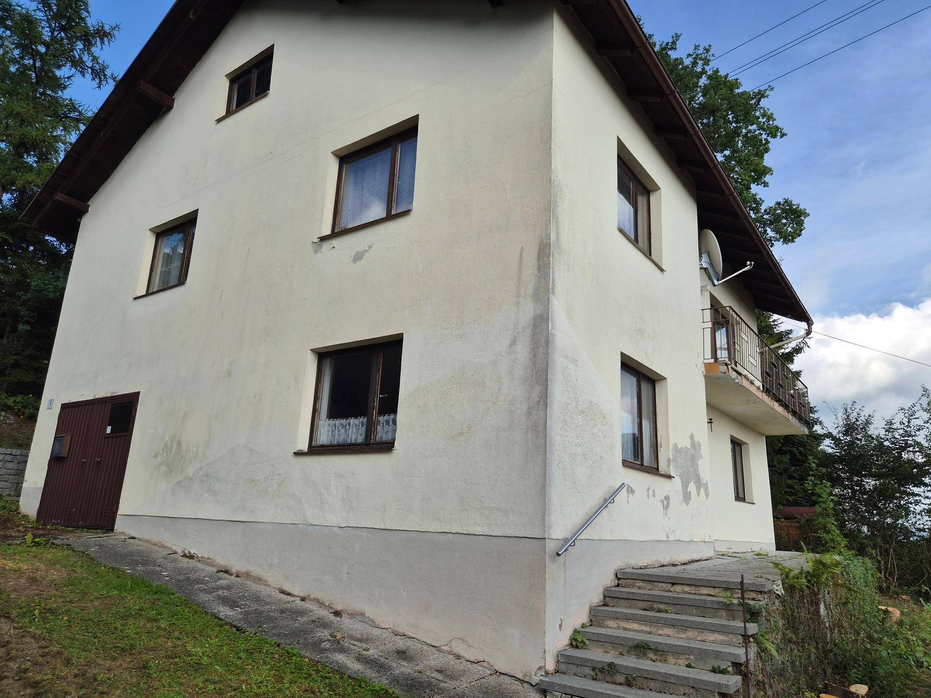 Außenansicht eines Hauses mit heller Fassade, braunen Fenstern und einem kleinen Balkon.