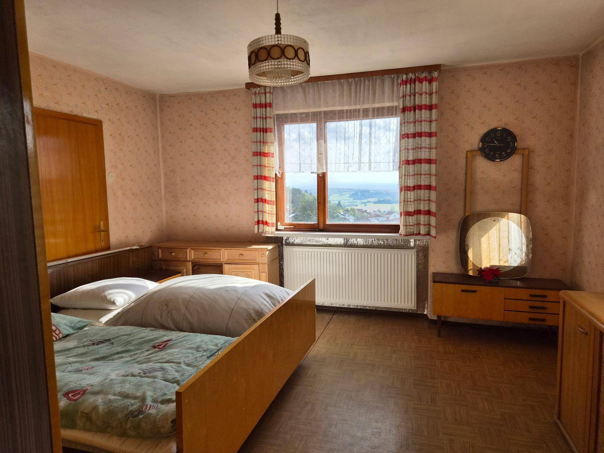 Schlafzimmer mit Einzelbett, Holzmöbeln und Fenster mit weitem Blick über die Landschaft.