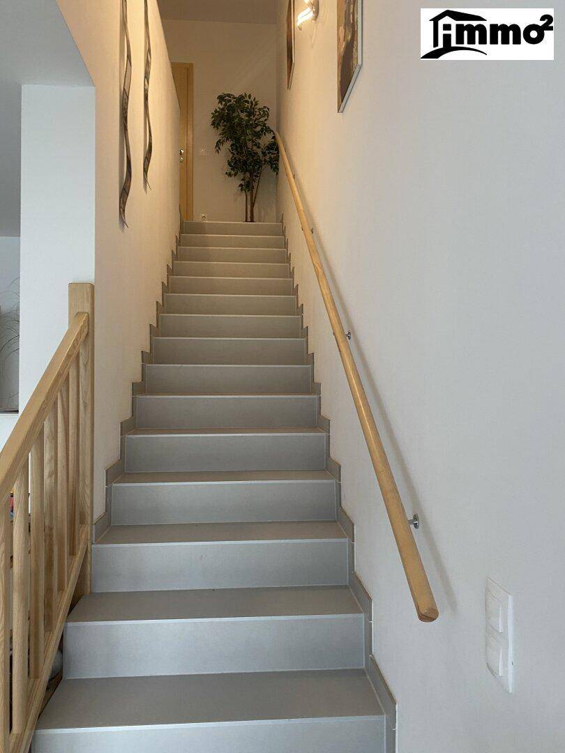 Treppenhaus mit hellem Holzgeländer und Stufen, die in die obere Etage führen.