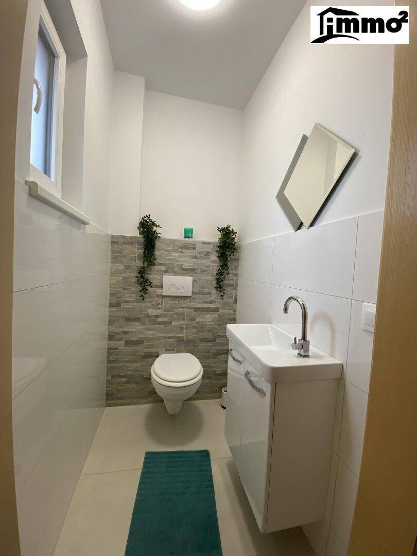Gäste-WC mit modernem Design, wandmontierter Toilette und kleinem Waschbecken.