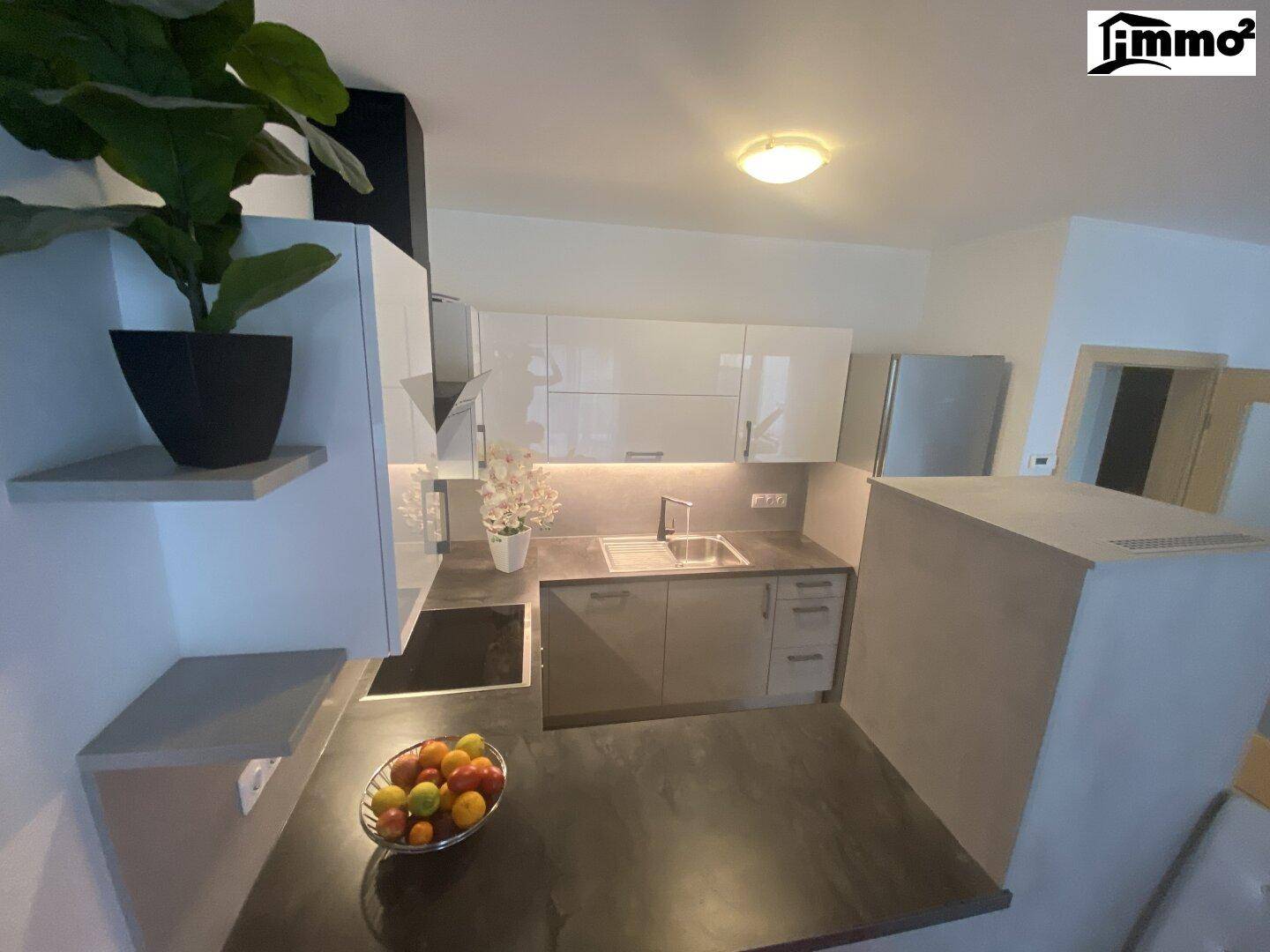 Moderne Küche mit weißen Hochglanzschränken, dunkler Arbeitsplatte und Induktionskochfeld.