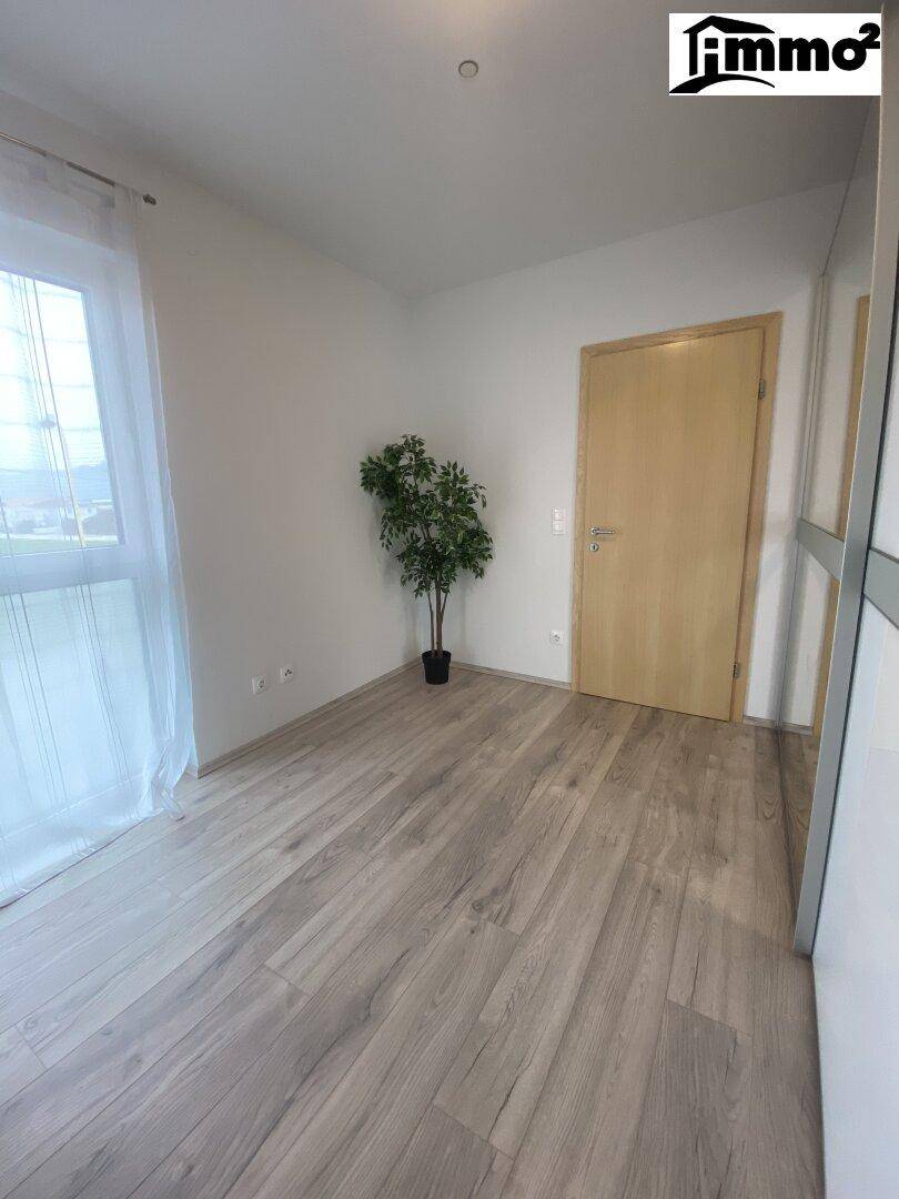 Helles Schlafzimmer mit Laminatboden und einer Tür, die zu einem weiteren Raum führt.