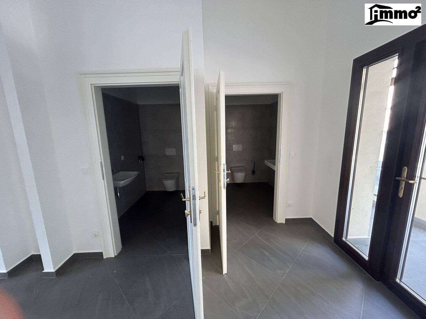 Innenraum mit Zugang zu zwei separaten Toilettenbereichen und einer großen Glastür zum Außenbereich.