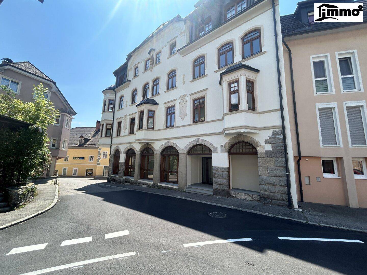 Gebäudeansicht von der Straße aus, mit klassischer Fassade und umliegenden Häusern unter strahlendem Himmel.