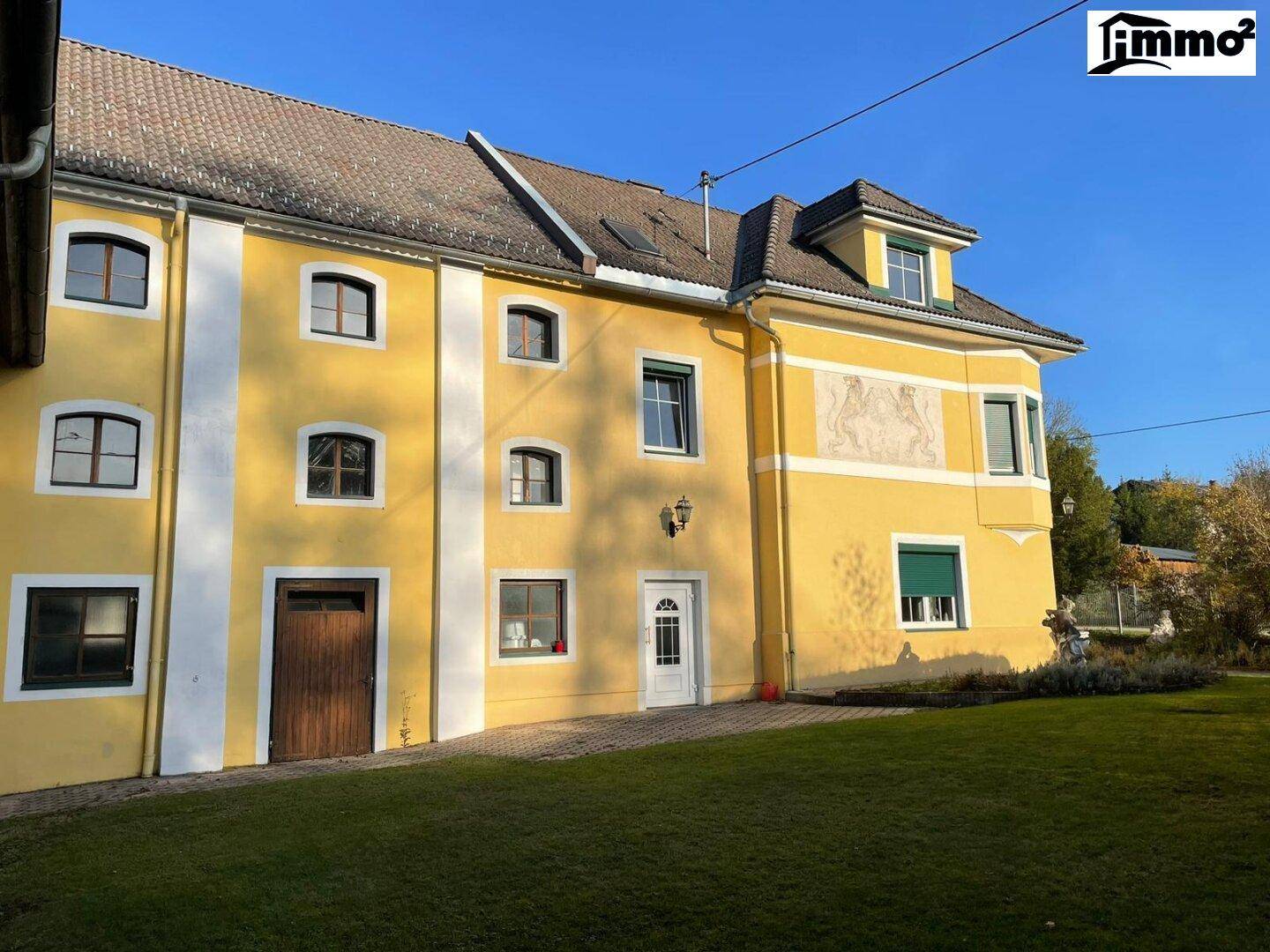 Gelbe Fassade eines traditionellen Gebäudes mit gepflegtem Rasen und dekorativen Elementen.
