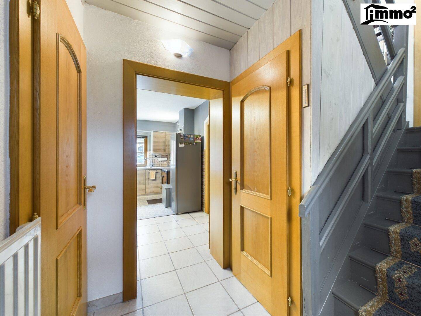 Heller Flur mit Fliesenboden, Holztreppe und Zugang zu weiteren Räumen.