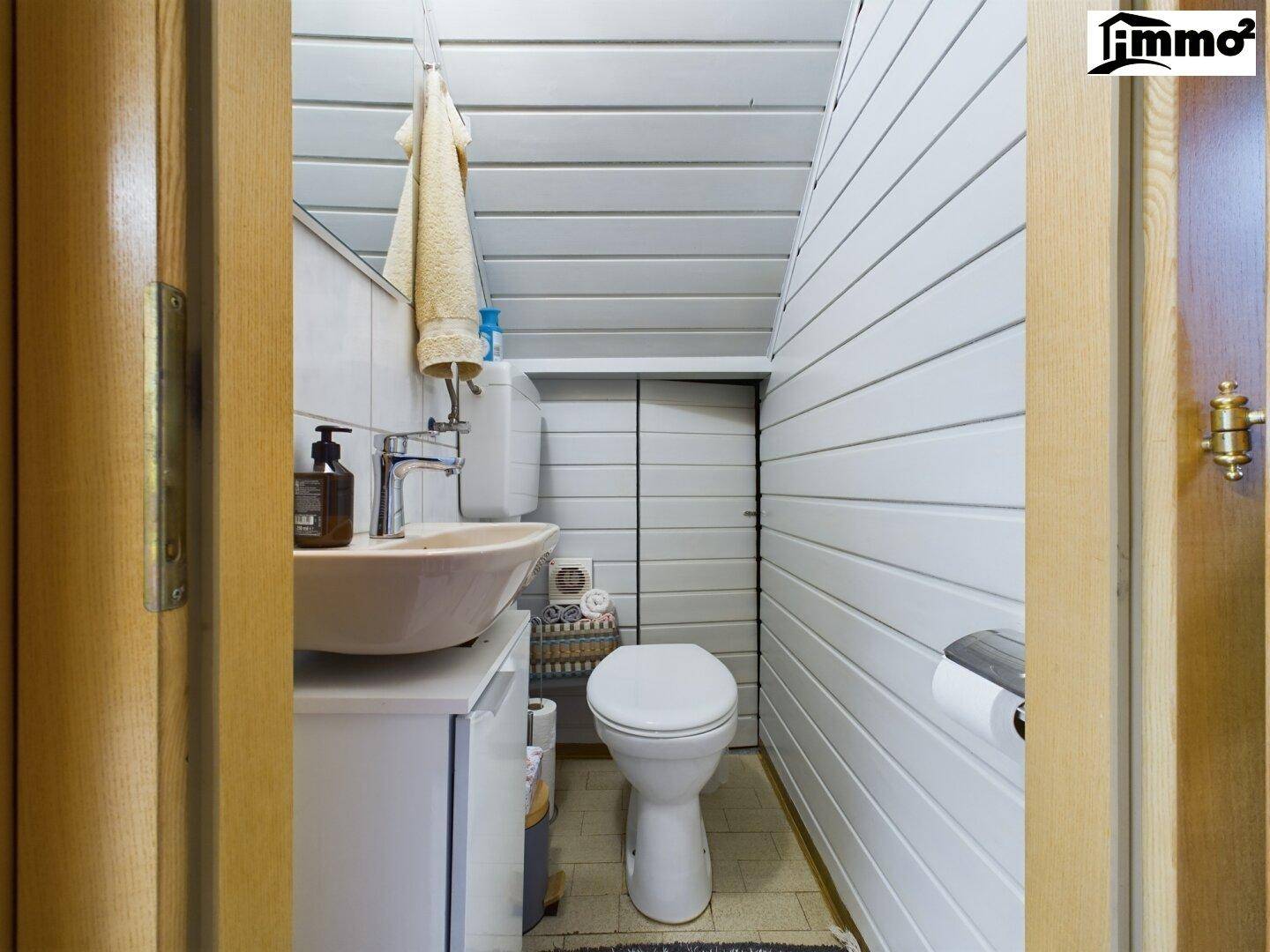 Kleines Gäste-WC mit Waschbecken, Toilette und Holzverkleidung an den Wänden.