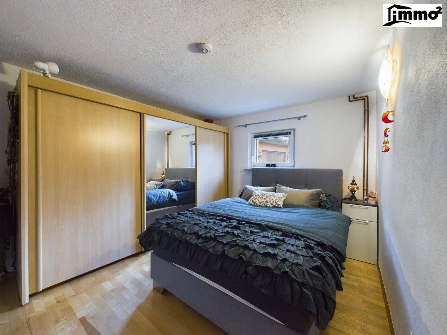 Schlafzimmer mit Holzboden, großem Bett und Spiegelschiebetüren am Kleiderschrank.
