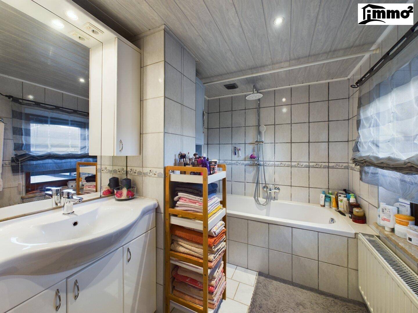 Badezimmer mit Badewanne, Waschbecken und Spiegelschrank, hell gefliest.