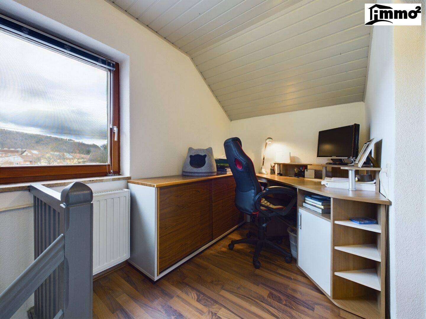 Dachgeschoss-Büro mit Holzboden, Schreibtisch und Blick aus dem Fenster.
