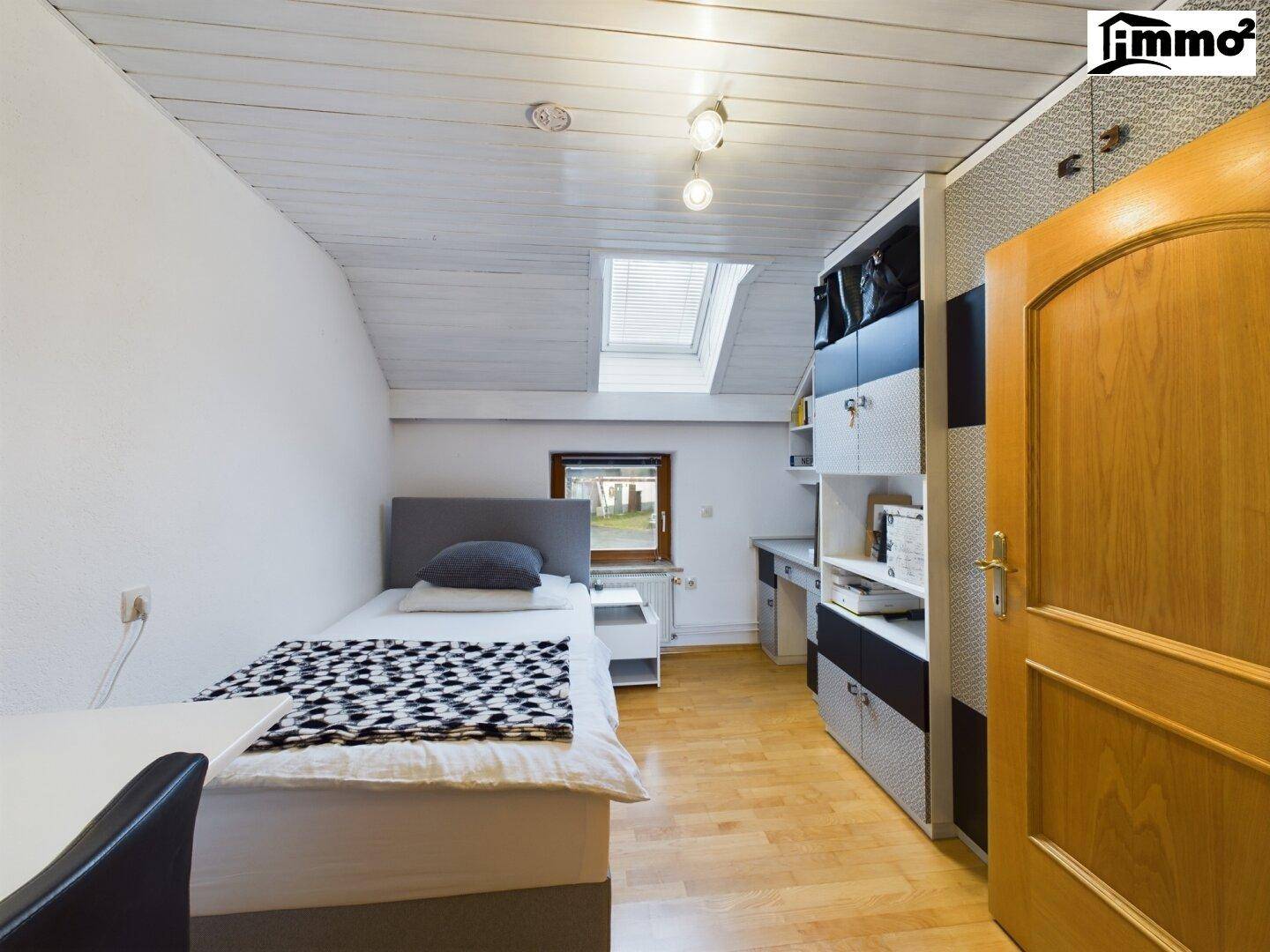 Helles Schlafzimmer im Dachgeschoss mit Einzelbett, Schreibtisch und Dachfenster.