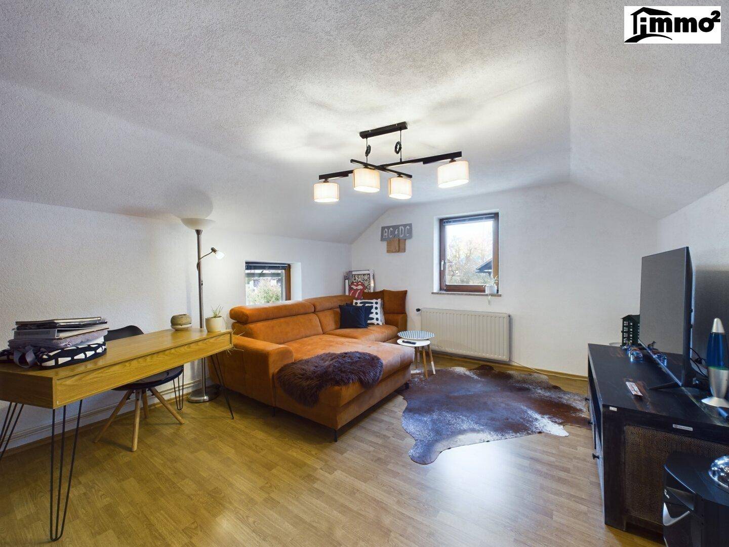 Geräumiges Wohnzimmer im Dachgeschoss mit Holzboden, Sofa und mehreren Fenstern.