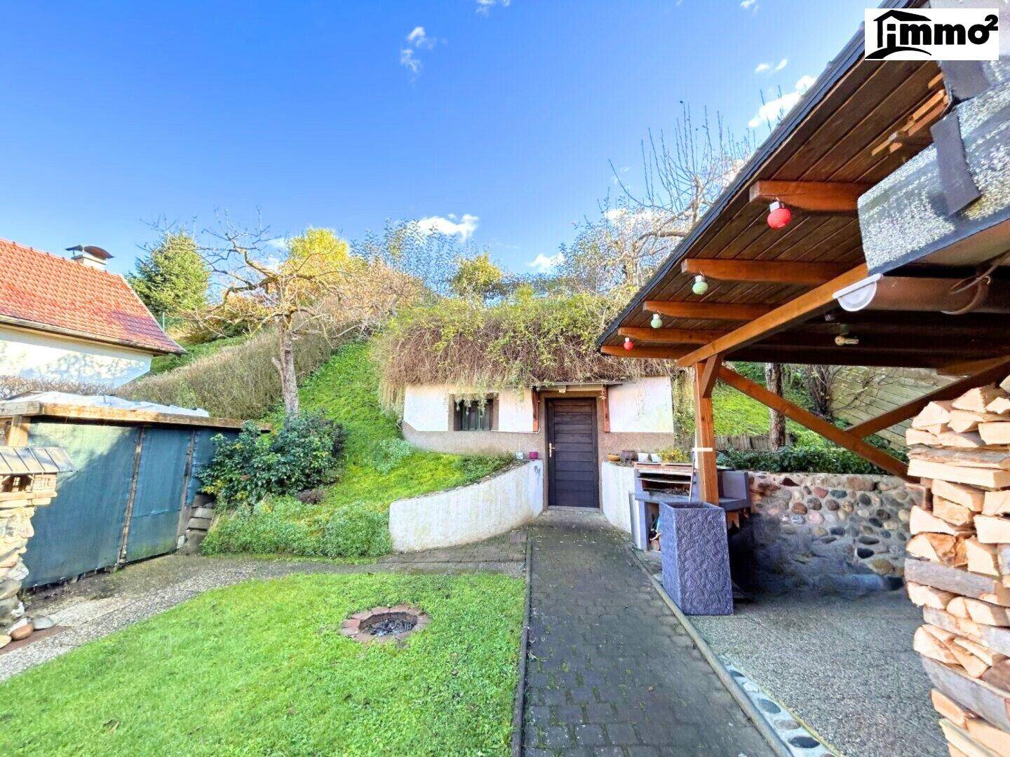 Garten mit Rasenfläche, überdachtem Bereich und einem in den Hang gebauten Keller.