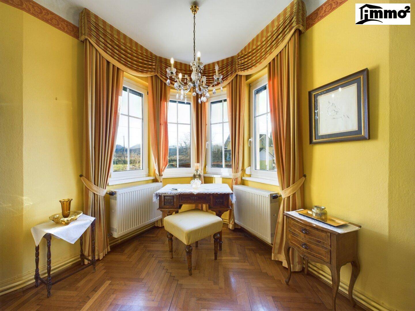 Gemütliche Ecke mit Schreibtisch, Parkettboden und großen Fenstern, die viel Tageslicht hereinlassen.