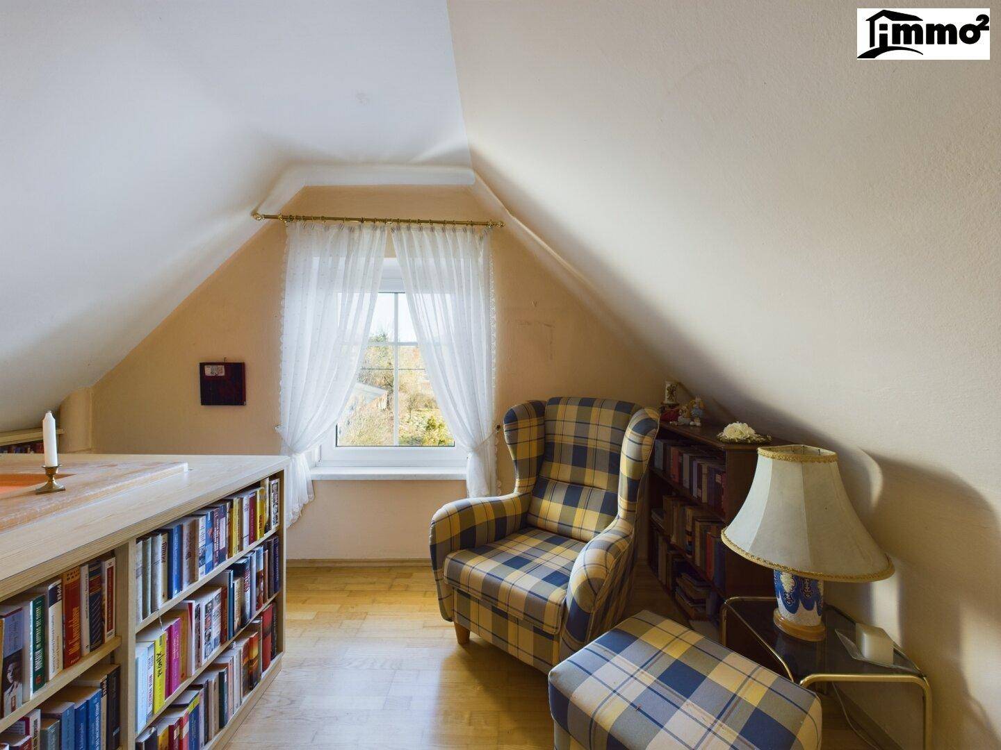 Helle Leseecke im Dachgeschoss mit Bücherregalen, Sessel und Fenster mit Blick ins Grüne.