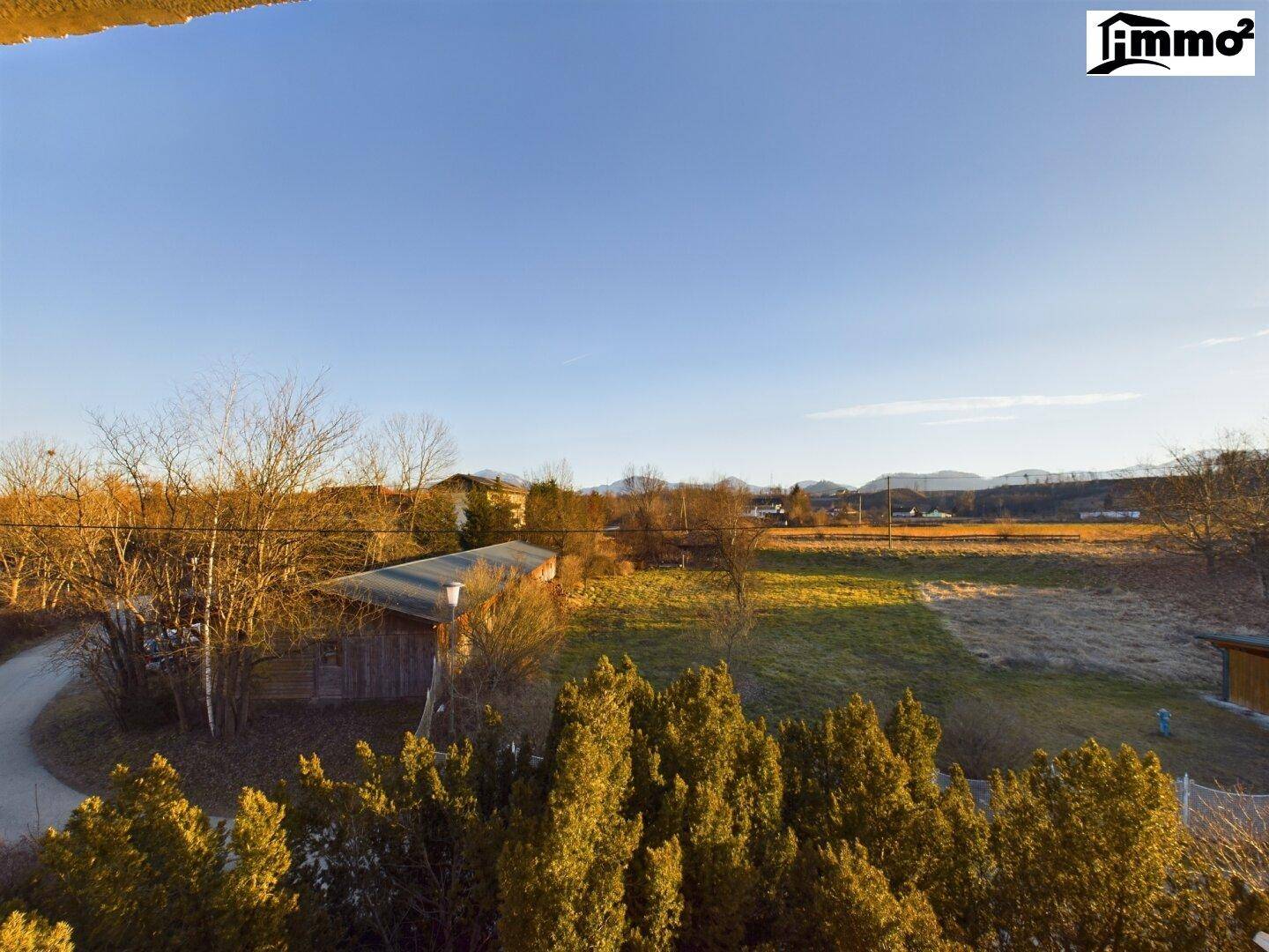 Weitläufiger Blick über Felder und Bäume bis zu den fernen Bergen unter klarem Himmel.