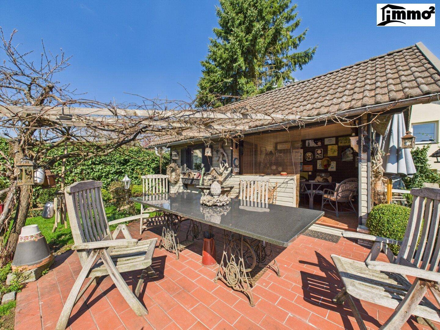 Gemütliche Terrasse mit Pergola, Esstisch und Holzstühlen im sonnigen Gartenbereich.