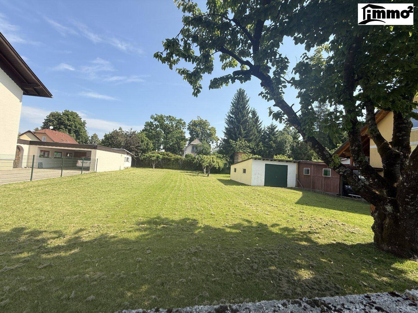 Gepflegter Garten mit altem Baumbestand, Rasenfläche und einem kleinen Schuppen unter strahlendem Sonnenschein.