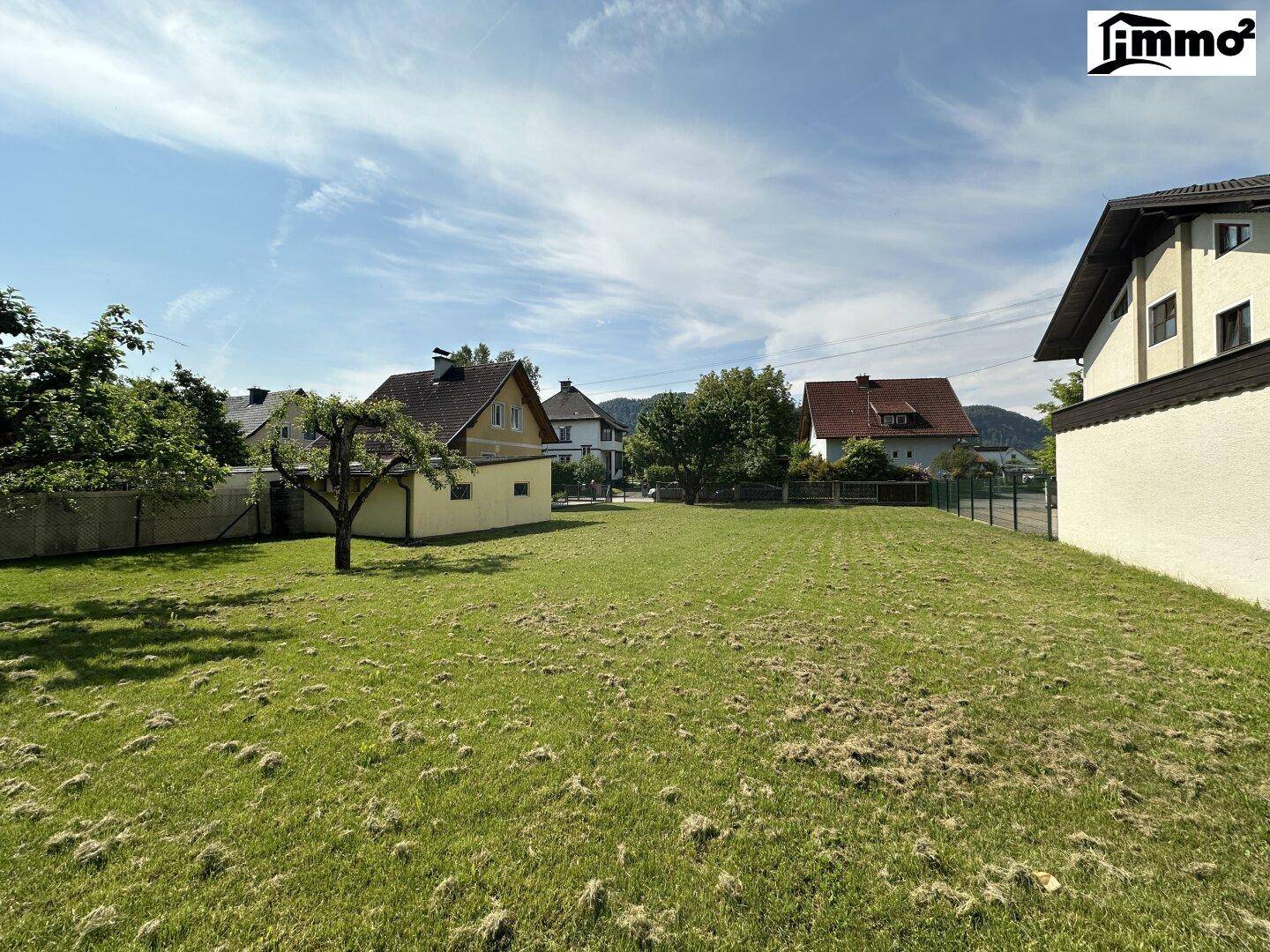 Offenes Gartengrundstück mit weitem Rasen, umgeben von Wohnhäusern und Bäumen unter klarem Himmel.