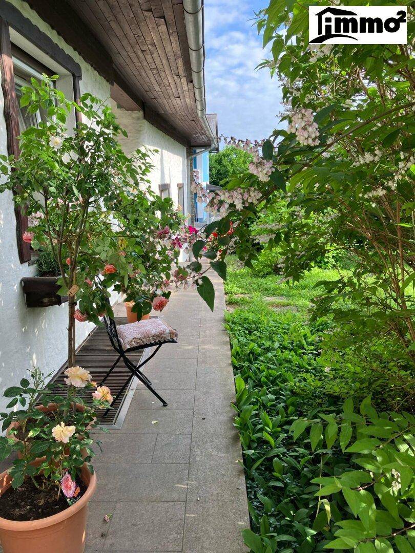 Seitlicher Gartenweg entlang des Hauses, gesäumt von blühenden Pflanzen und Sträuchern.