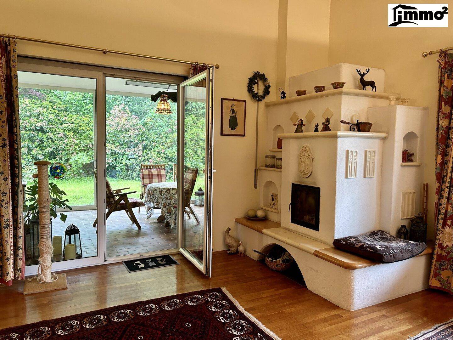 Helles Wohnzimmer mit traditionellem Kachelofen und Zugang zur Terrasse mit Gartenblick.