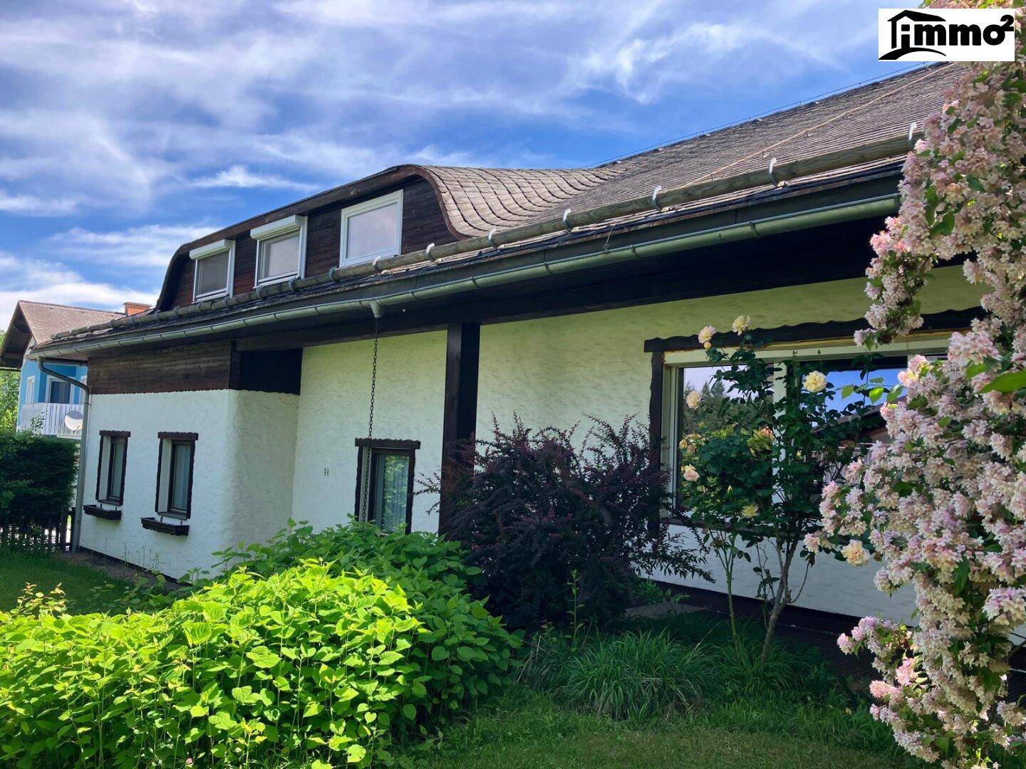 Seitenansicht des Hauses mit gepflegtem Garten und blühenden Büschen unter blauem Himmel.