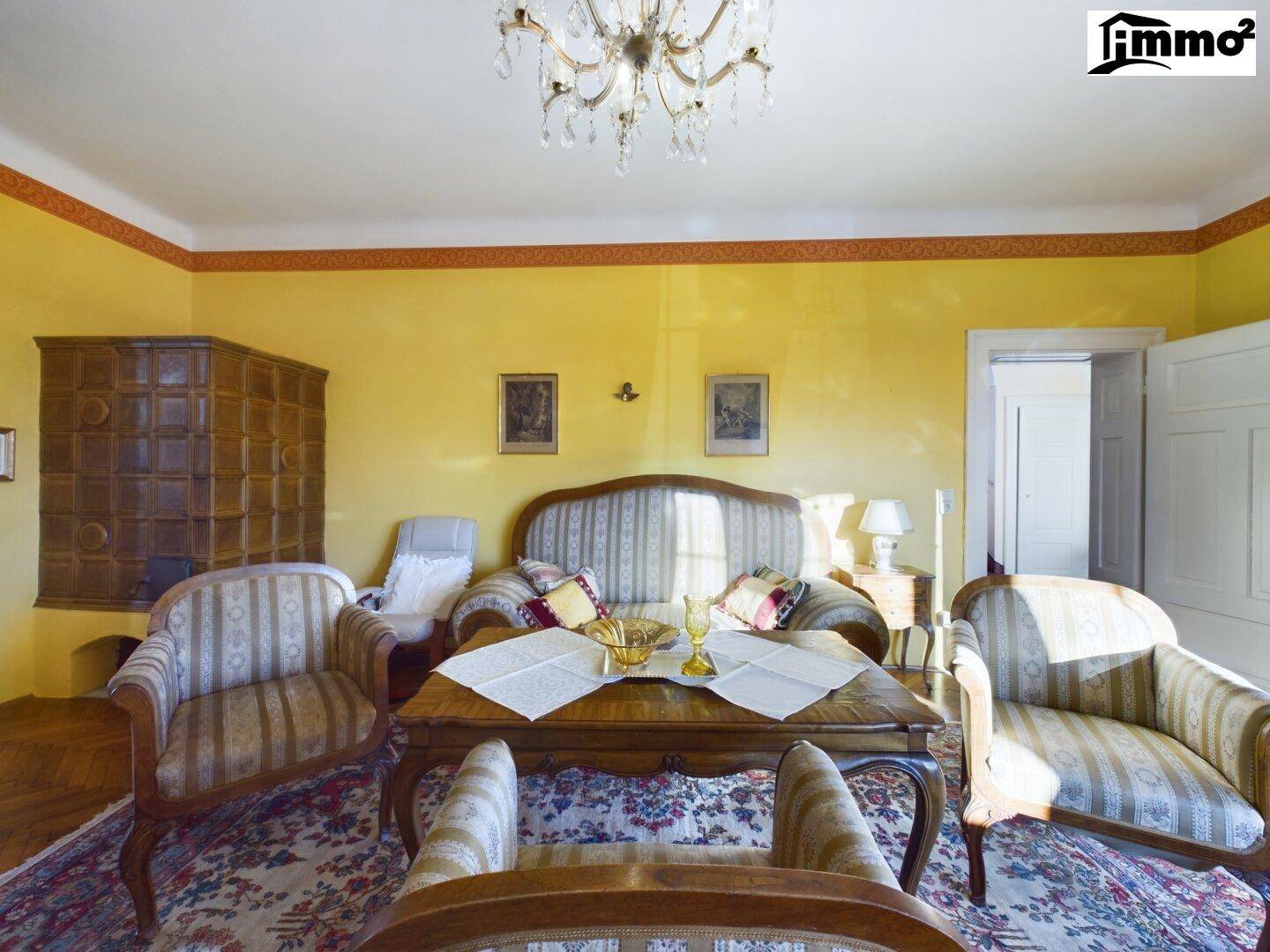Gemütliches Wohnzimmer mit traditionellem Kachelofen, eleganten Möbeln und Kronleuchter.